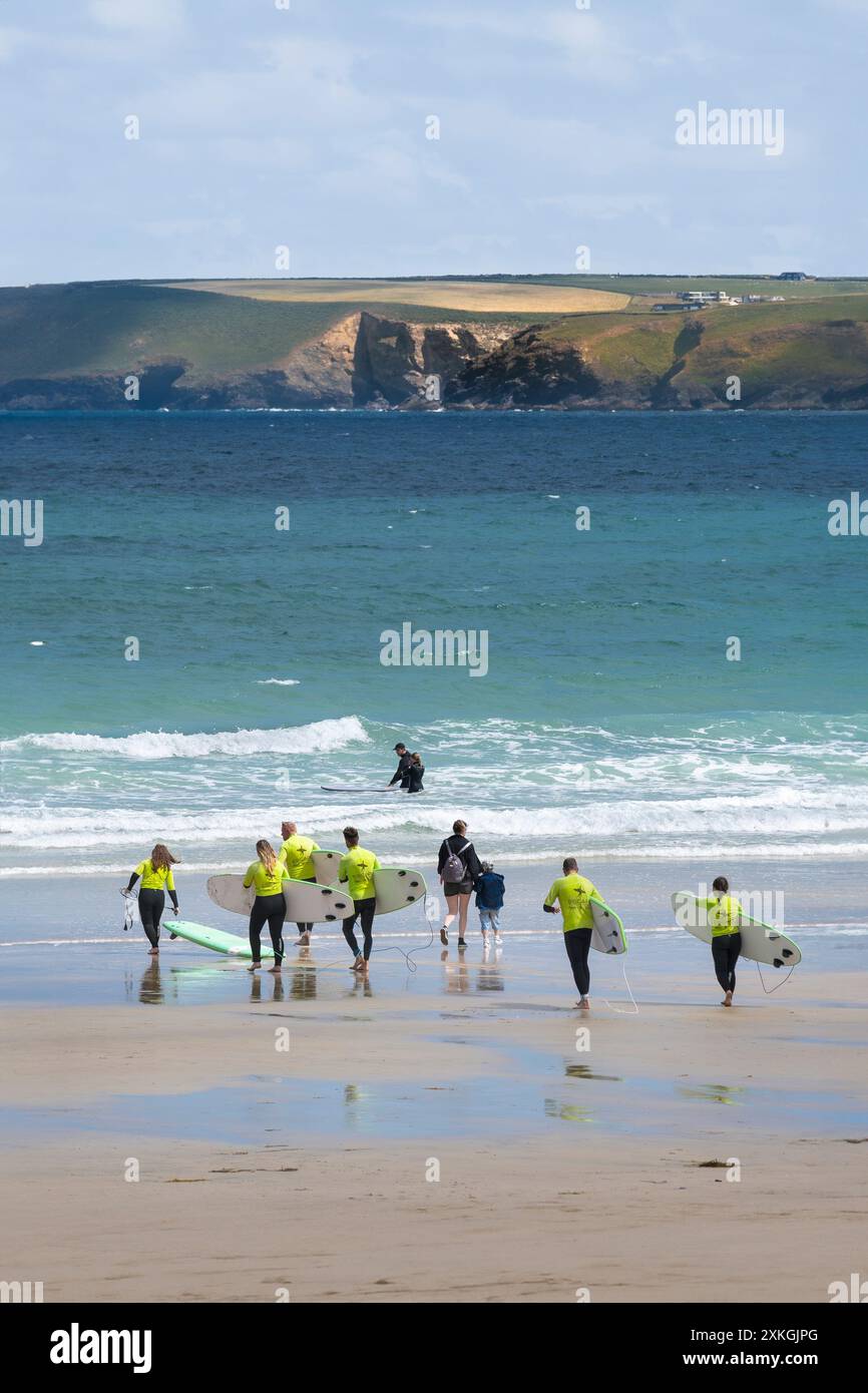 I principianti della Escape Surf School camminano in mare per una lezione di surf a Towan Beach a Newquay in Cornovaglia nel Regno Unito. Foto Stock