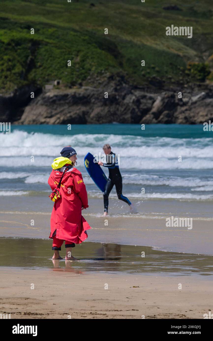Un bagnino della Royal National Lifeboat Institution della RNLI, in servizio sulla riva, osservando i surfisti principianti che tengono una lezione di surf in mare a Towan Foto Stock