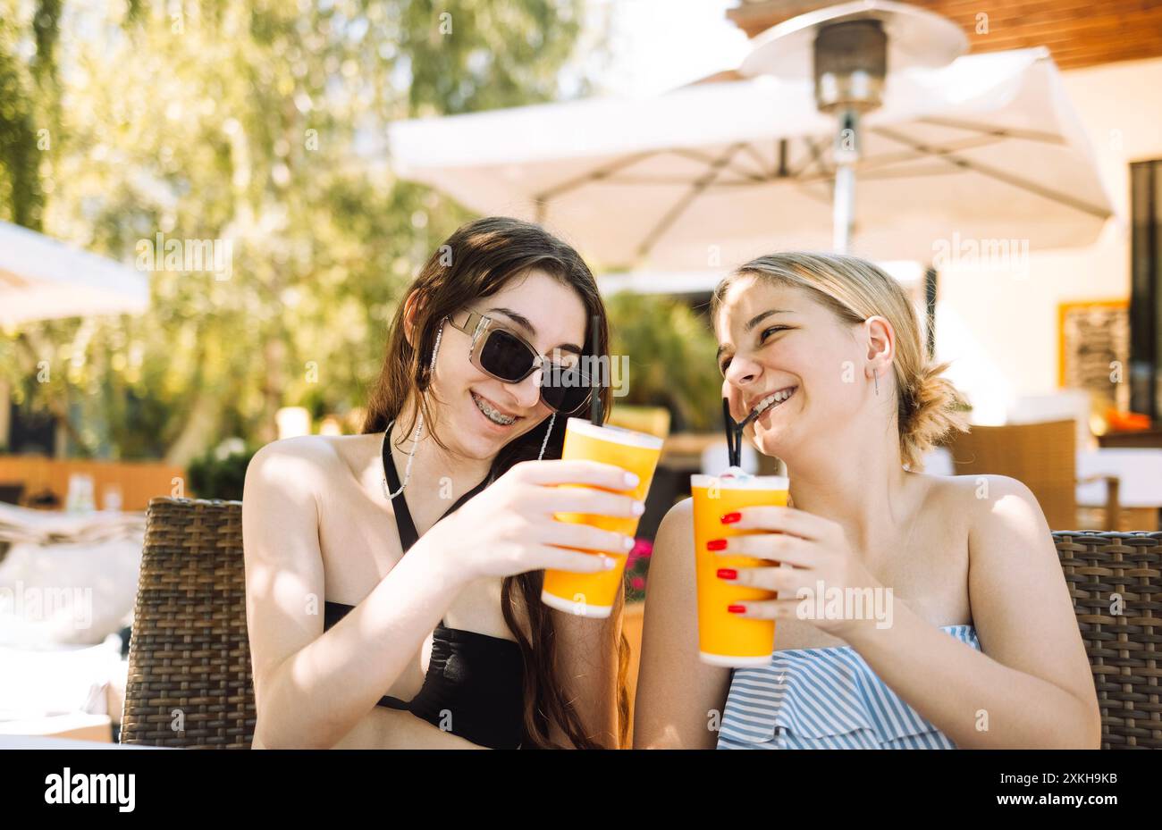 Due adorabili amici in costume da bagno bevono del delizioso succo di frutta fresco. Gli adolescenti allegri alzano un brindisi e si spalancano i bicchieri con la limonata. rel. Ragazze spensierate Foto Stock