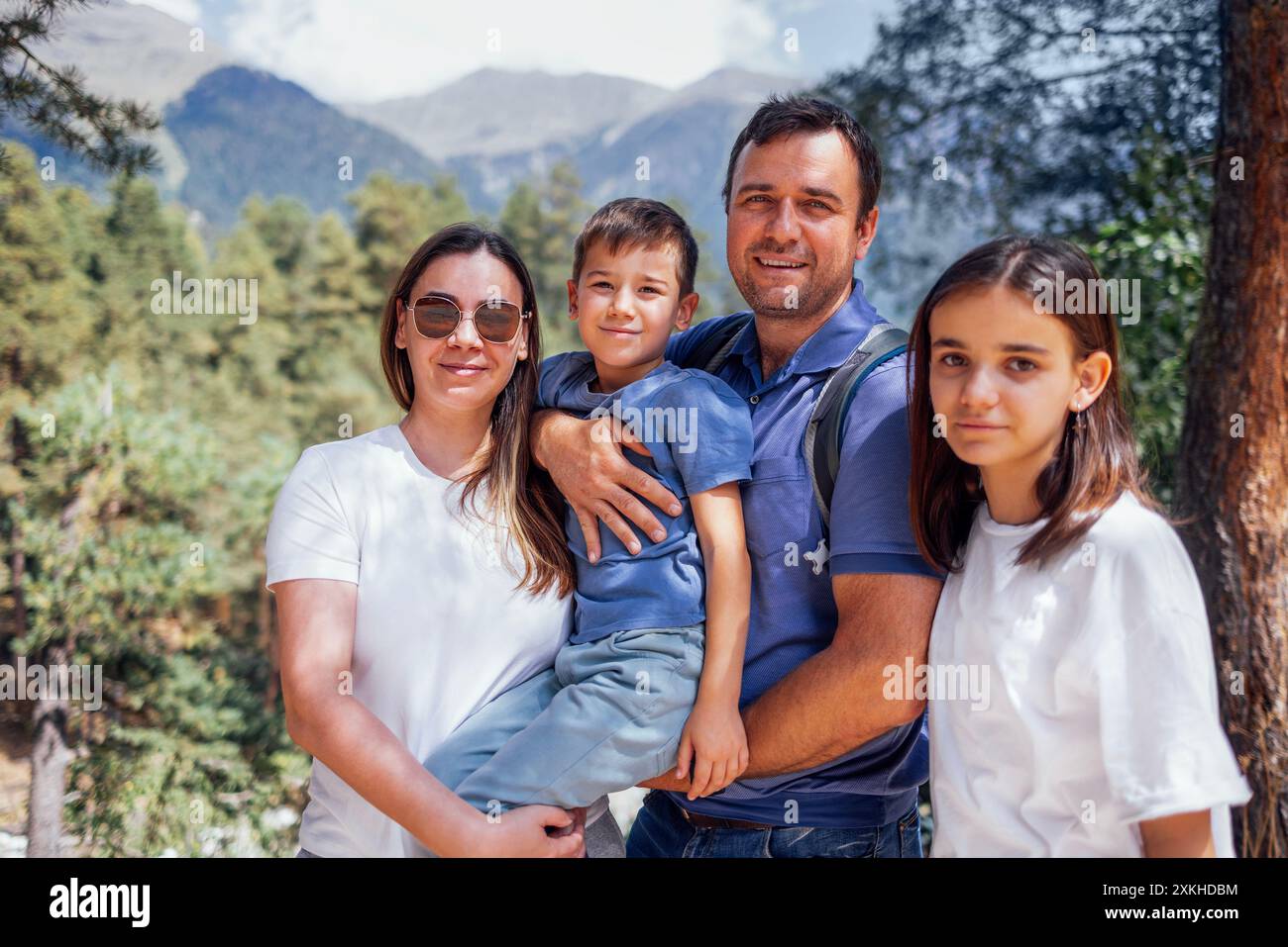 Famiglia felice sullo sfondo del paesaggio montano. Giovani coppie sposate con il loro figlio e figlia stanno camminando nella foresta. I turisti sorridenti amano la natura Foto Stock