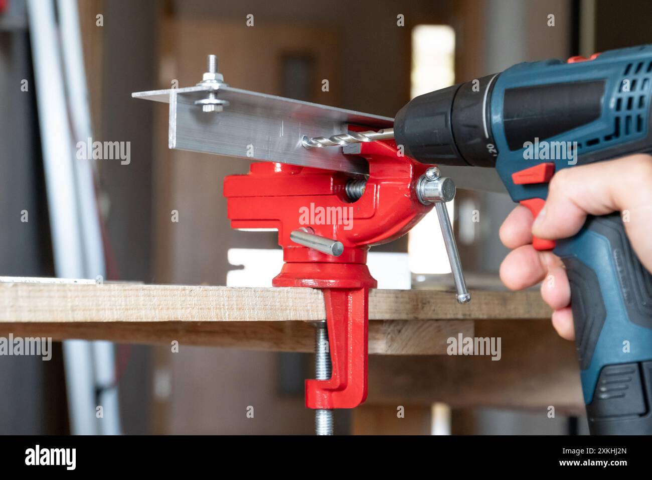Mano maschio con un cacciavite elettrico utilizzato come trapano fori nei dettagli in alluminio inseriti in una morsa per fabbro. Concetto di riparazione della casa Foto Stock