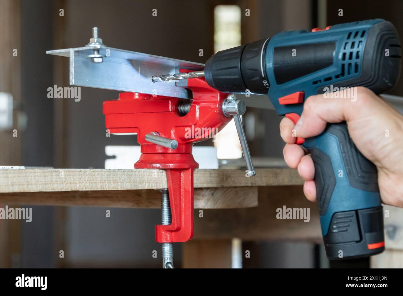 Mano maschio con un cacciavite elettrico utilizzato come trapano fori nei dettagli in alluminio inseriti in una morsa per fabbro. Concetto di riparazione della casa Foto Stock