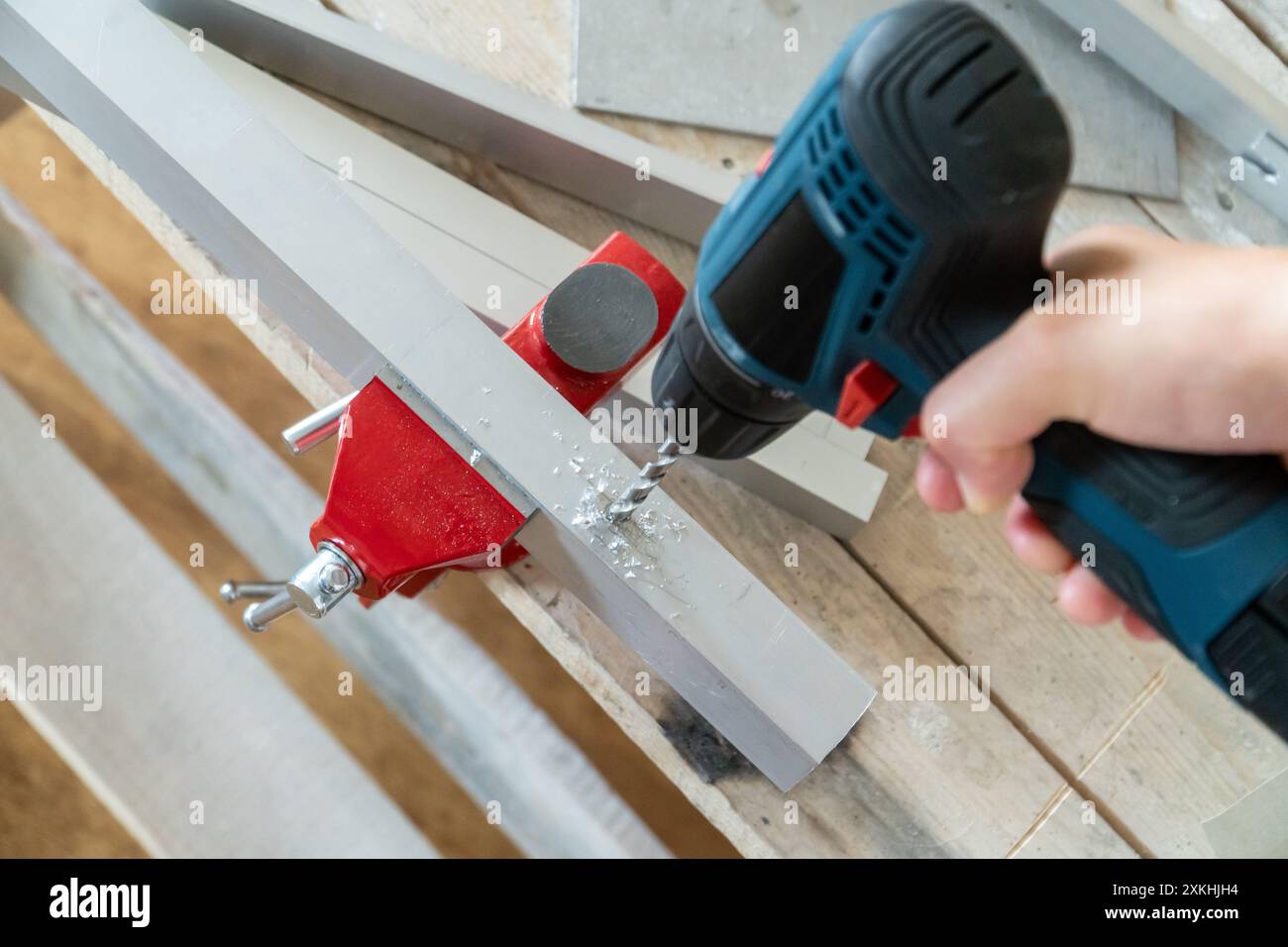 Mano maschio con un cacciavite elettrico utilizzato come trapano fori nei dettagli in alluminio inseriti in una morsa per fabbro. Concetto di riparazione della casa Foto Stock