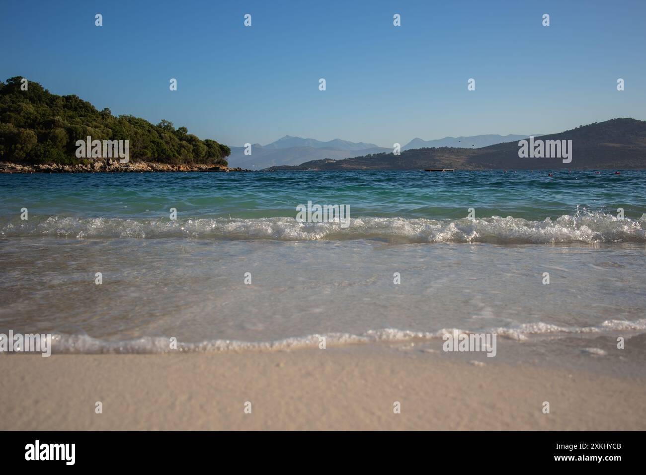 Paesaggio mattutino di Sandy Shore con il Mar Ionio e l'isola di Ksamil nel sud dell'Albania. Paesaggio albanese dell'acqua e delle montagne durante la mattina d'estate. Foto Stock