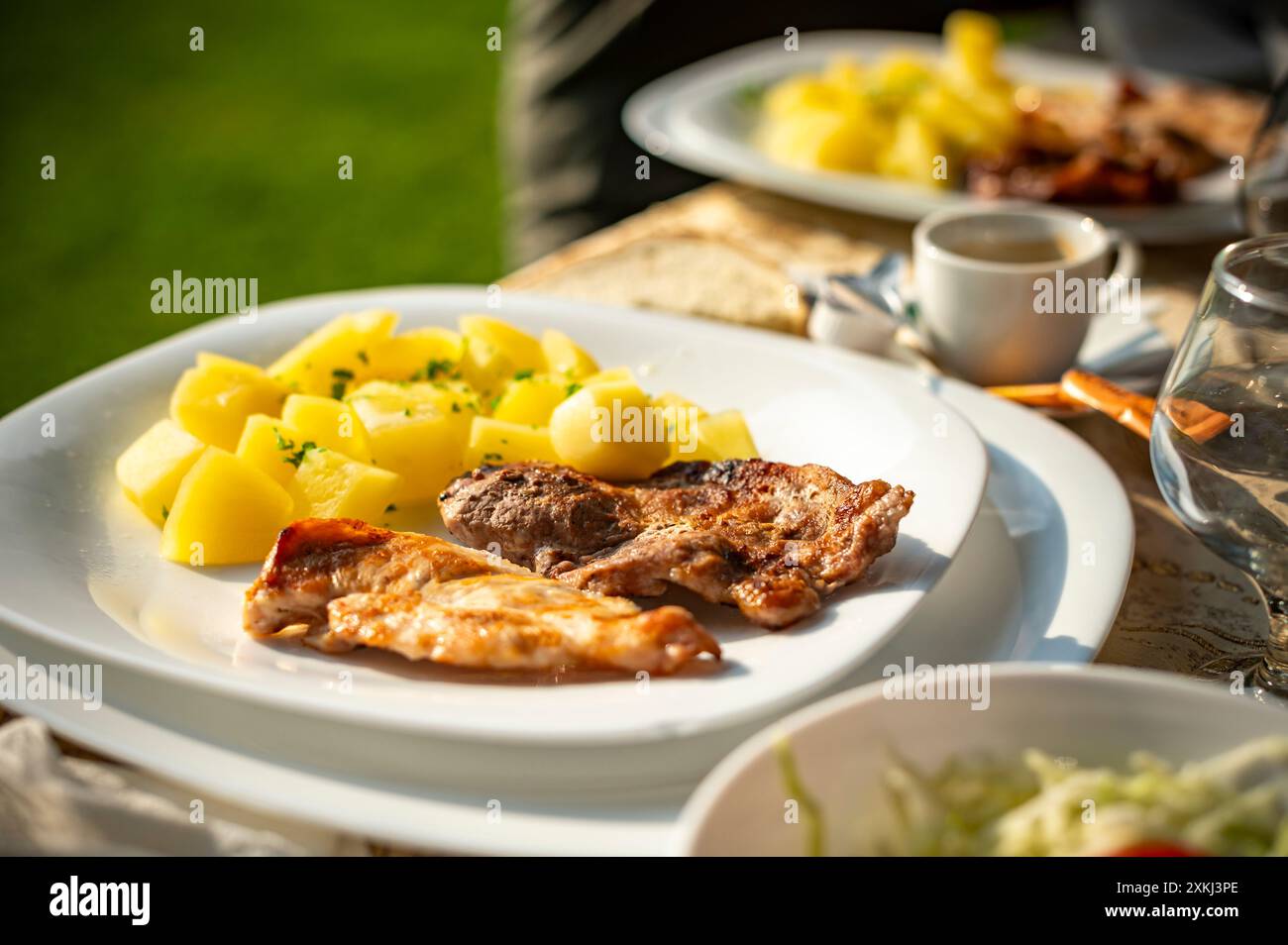 menu semplice e gustoso, patate naturali imbevute di burro e aromatizzate con prezzemolo e maiale alla griglia, a una festa in giardino nel pomeriggio estivo Foto Stock