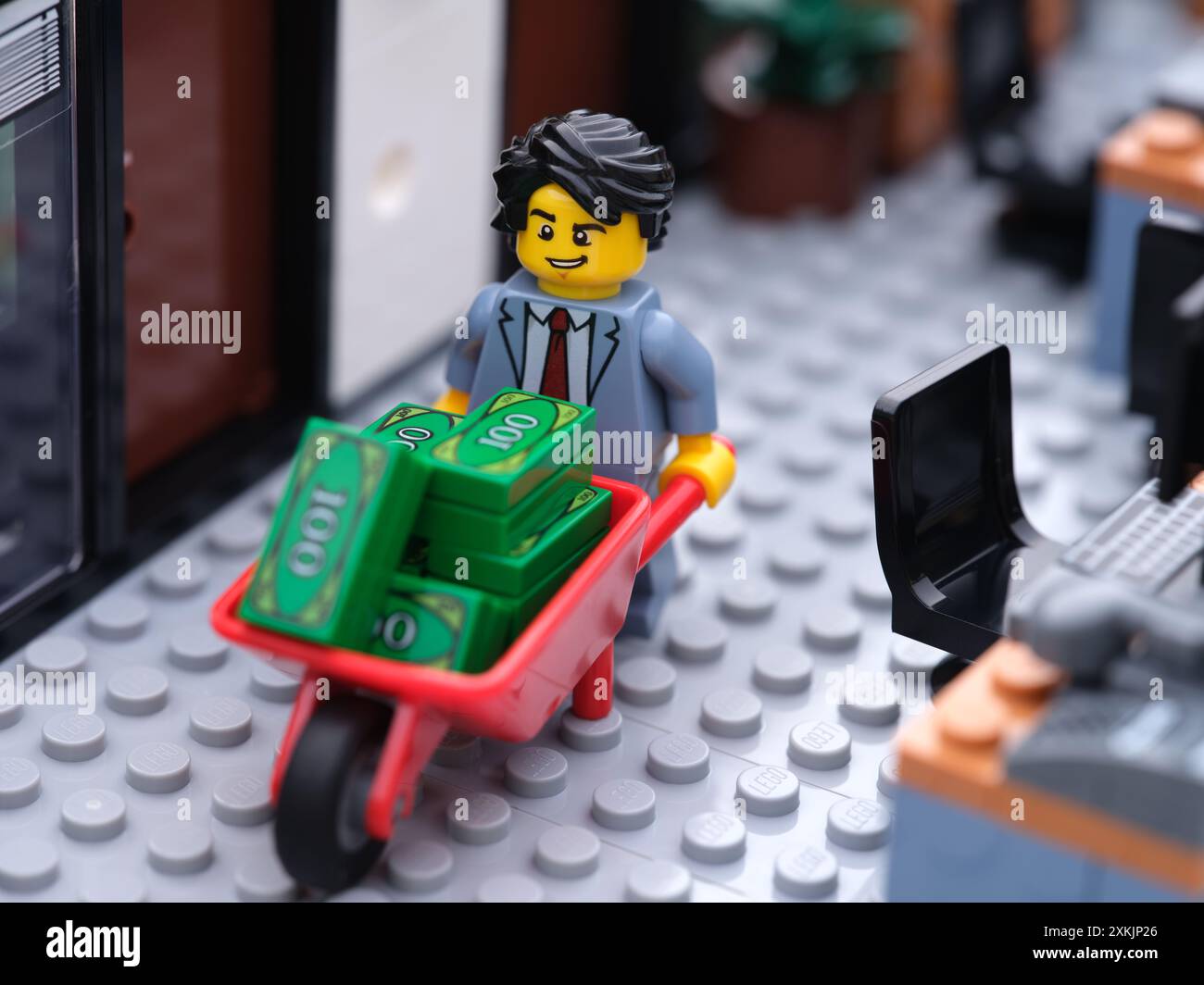 Tambov, Federazione Russa - 19 luglio 2024 Un uomo d'affari Lego che cammina in un ufficio e spinge una carriola piena di soldi. Foto Stock