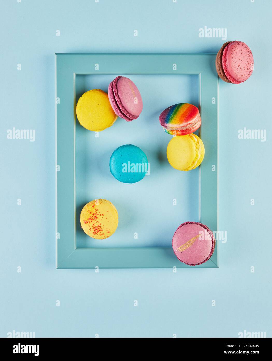 Macaron luminosi e colorati disposti all'interno e intorno a una cornice blu su sfondo azzurro. Foto Stock