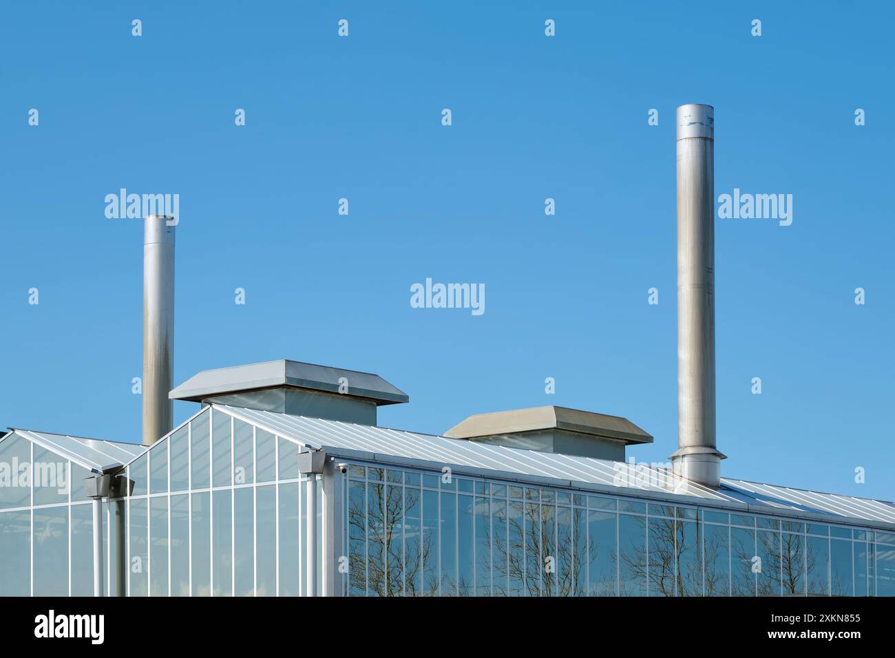 Tetto di una serra industriale con camini contro un cielo soleggiato blu. Immagine con spazio di copia Foto Stock