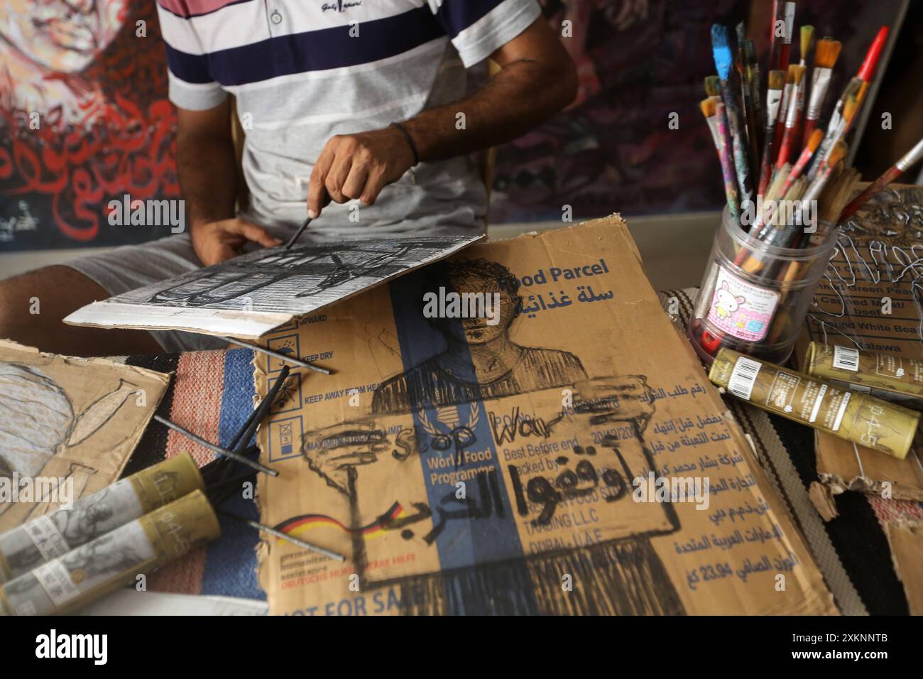 Un artista visivo palestinese Ahmed Muhanna dipinge dipinti all'interno del suo studio nel campo di Deir al-Balah Un artista visivo palestinese Ahmed Muhanna, dipinge dipinti all'interno del suo studio nel campo di Deir al-Balah, nella Striscia di Gaza centrale, il 24 luglio 2024. Al-Banna usa la carta delle scatole di cartone destinate a distribuire aiuti umanitari agli sfollati, per dipingere dipinti che esprimono la dura vita che i palestinesi vivono alla luce della continua guerra israeliana nella Striscia di Gaza. Foto di Naaman Omar apaimages Dair EL-Balah Striscia di Gaza territorio palestinese 240724 Dair El Balah NAA 0015 Copyright: xa Foto Stock