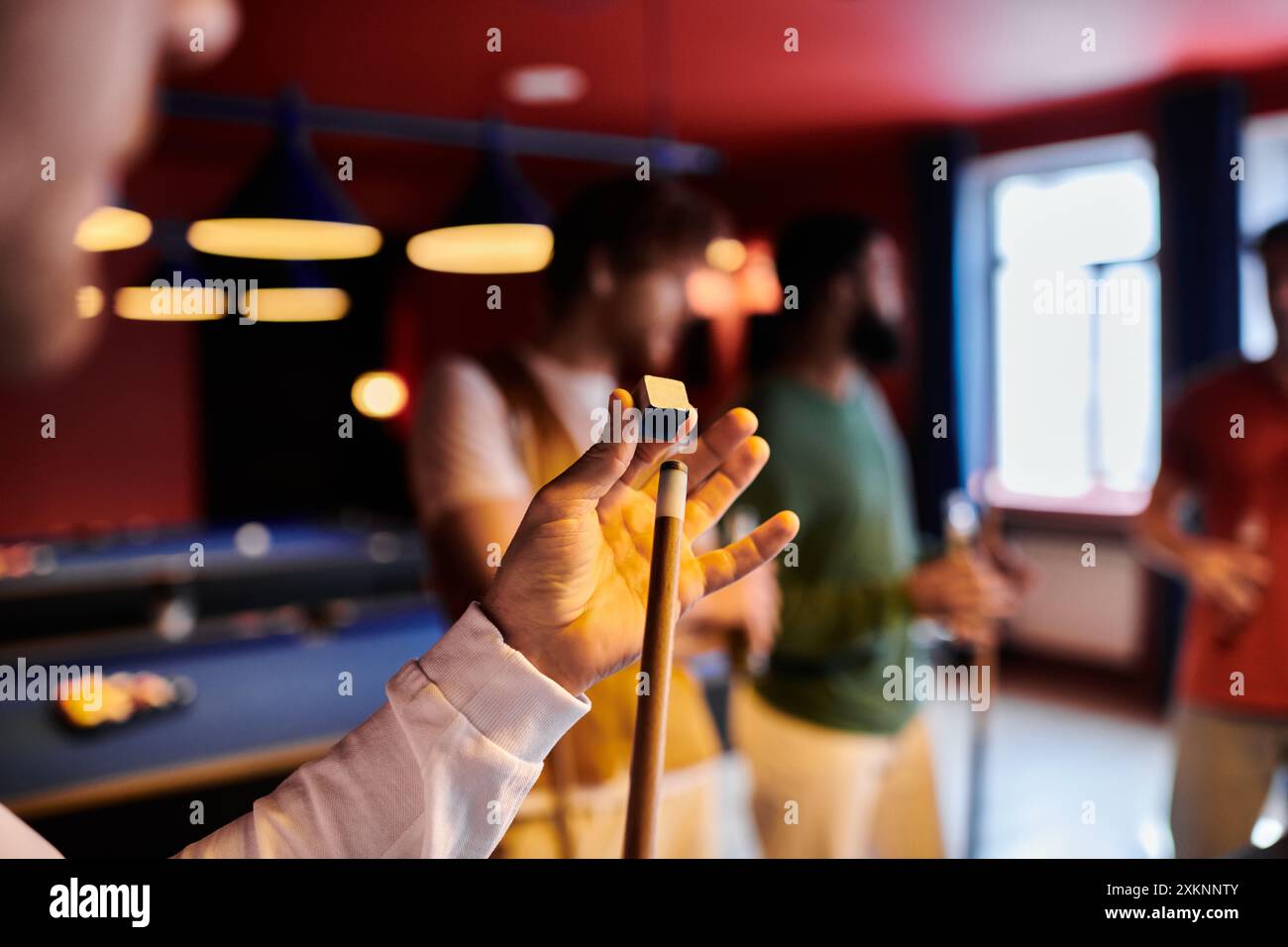 Un uomo tiene in mano un bastoncino e un gesso mentre gioca a biliardo con gli amici. Foto Stock