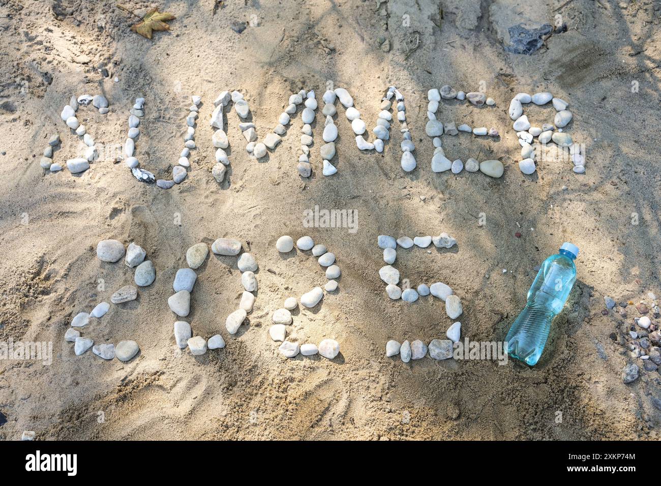 Text Estate 2025 scritto con ciottoli sulla sabbia sulla spiaggia e una bottiglia d'acqua, simbolo per il tempo libero, le vacanze al mare e bere abbastanza in un clima caldo Foto Stock