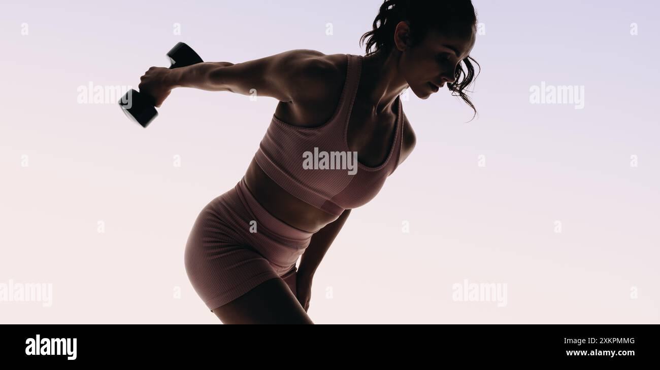 Una donna atletica solleva i pesi in uno studio, con particolare attenzione alla costruzione muscolare e all'allenamento di forza. Atleta femminile che utilizza manubri per un workou completo Foto Stock