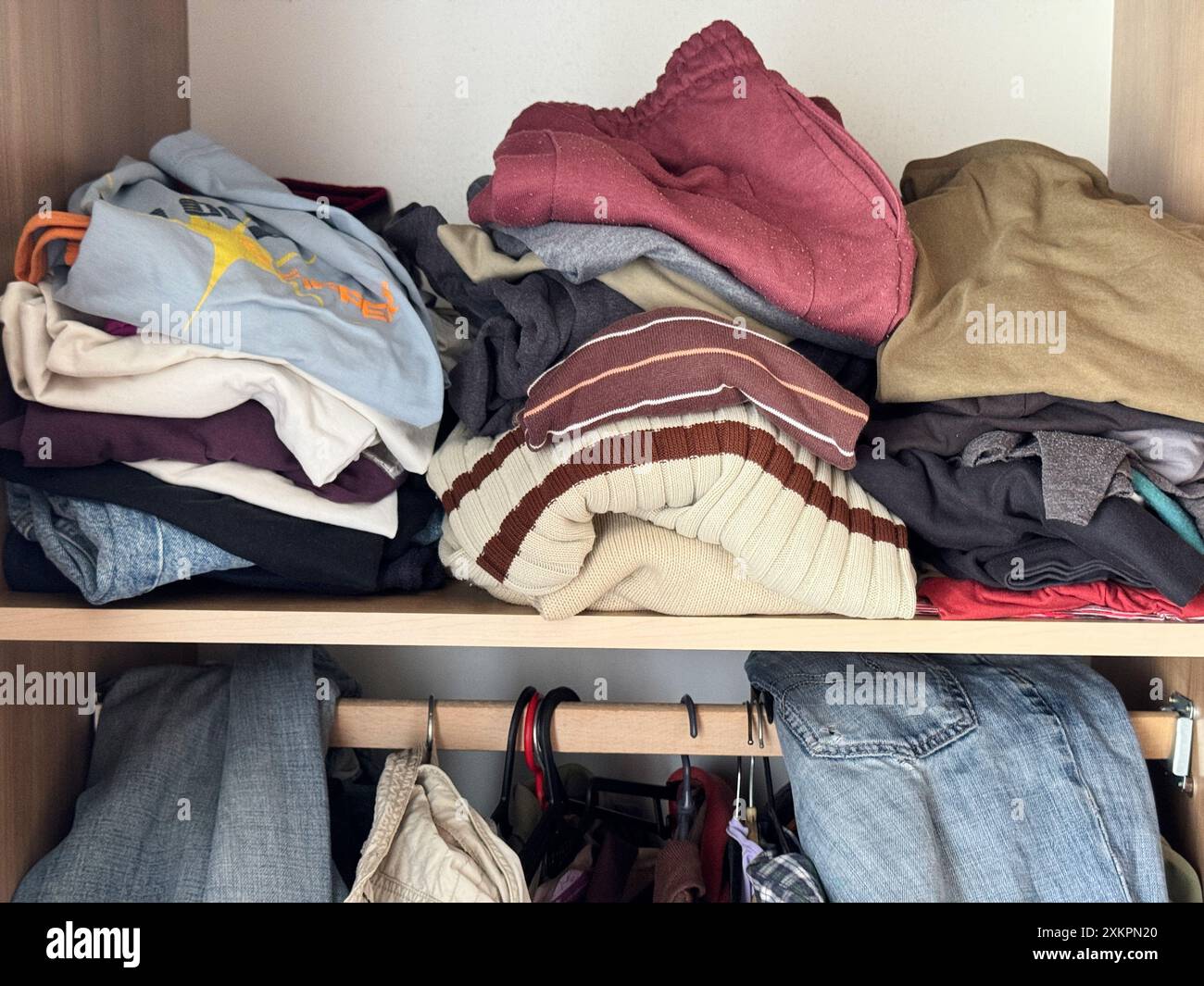 Armadio disordinato con abbigliamento casual assortito, maglioni e pantaloni su scaffali e grucce Foto Stock