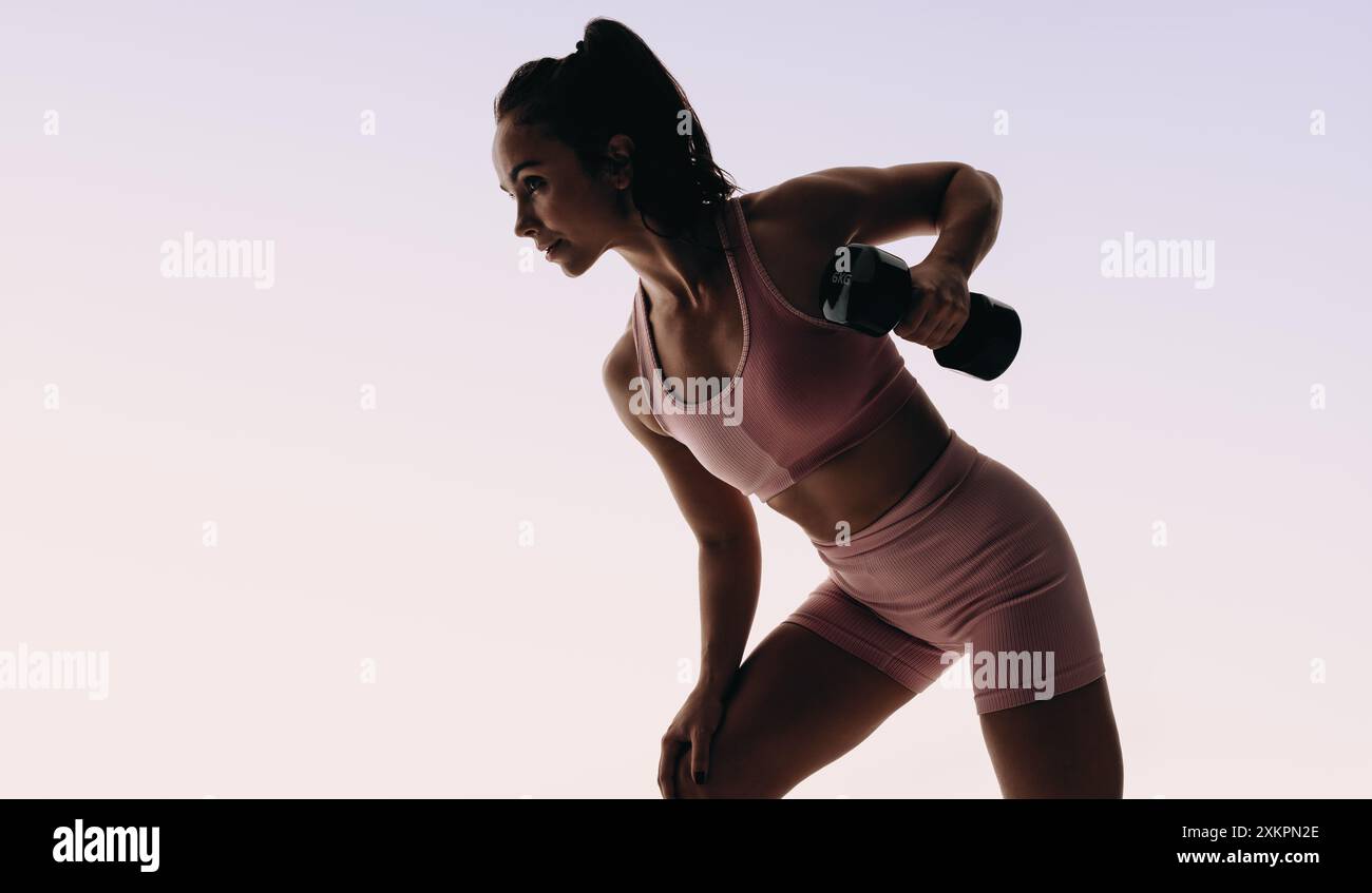 Una giovane donna si impegna in uno stile di vita attivo, esercitandosi in uno studio. Si concentra sulla costruzione di muscoli e forza, eseguendo routine di sollevamento pesi con intelligenza Foto Stock