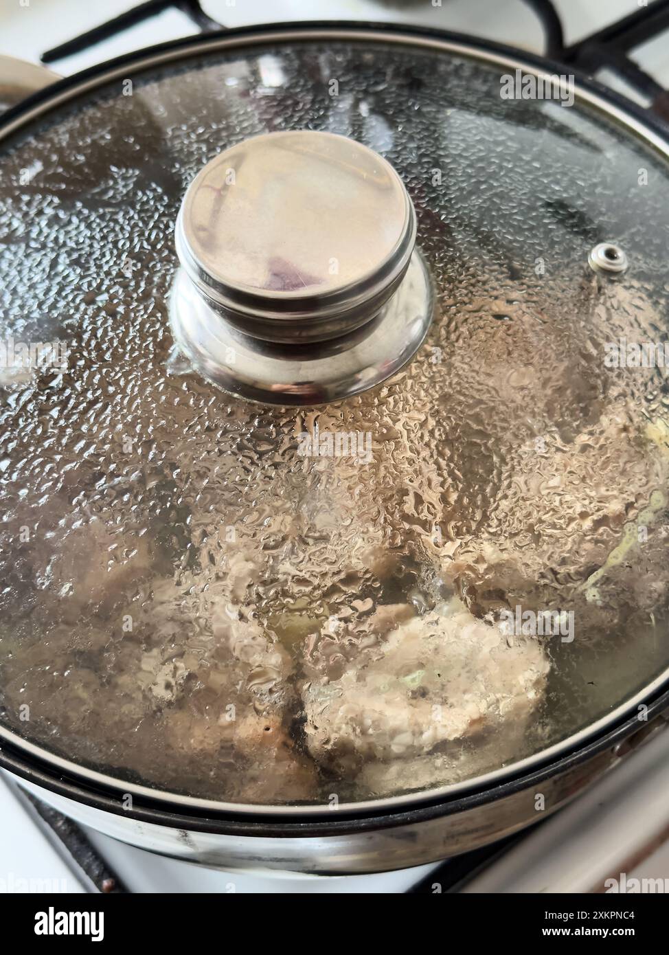 Pentola per cuocere a vapore su piano cottura con coperchio in vetro che mostra al suo interno la carne da cuocere Foto Stock