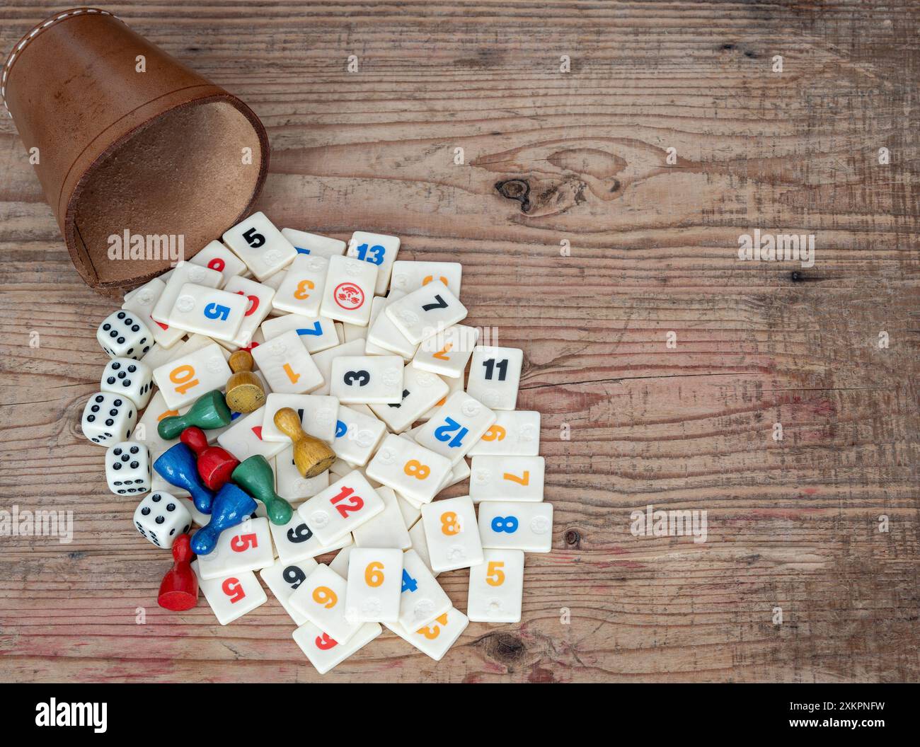 Classici giochi da tavolo, coppa in pelle con dadi e piastrelle rummikub su sfondo in legno Foto Stock
