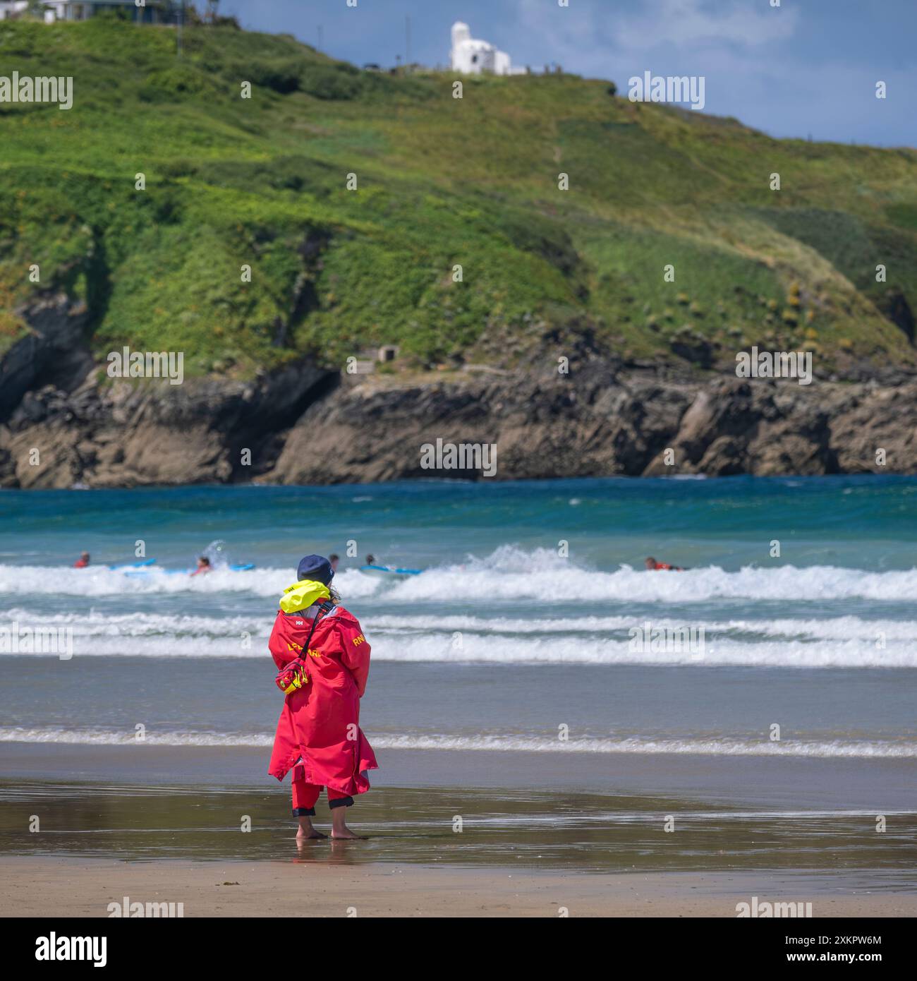 Un bagnino della Royal National Lifeboat Institution della RNLI, in servizio sulla riva, osservando i surfisti principianti che tengono una lezione di surf in mare a Towan Foto Stock