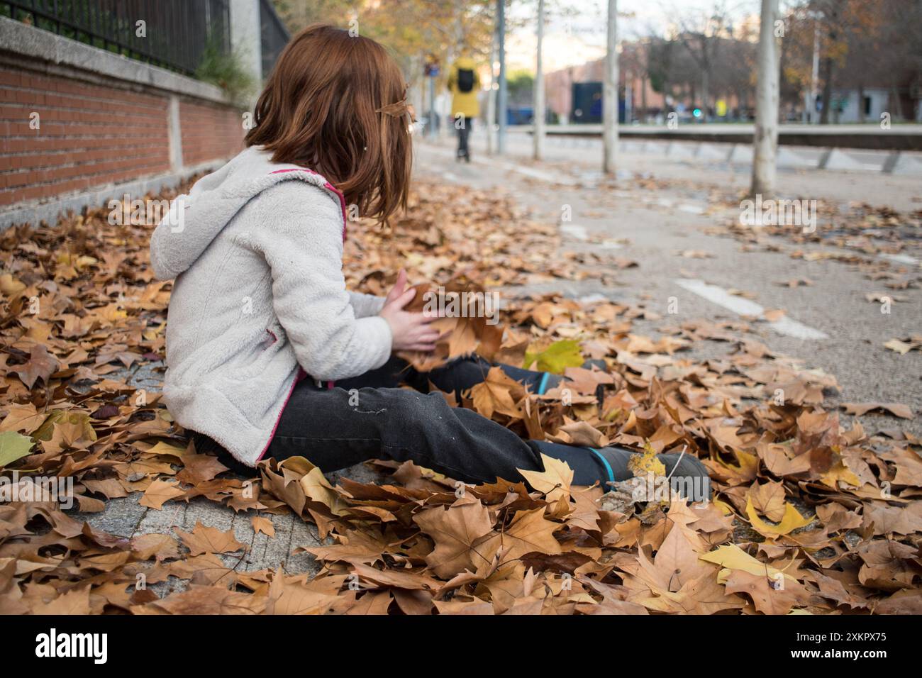 Ragazza seduta rilassarsi in foglie cadute in città autunnale guardando indietro una donna che cammina. Orizzontale. Ottobre Foto Stock