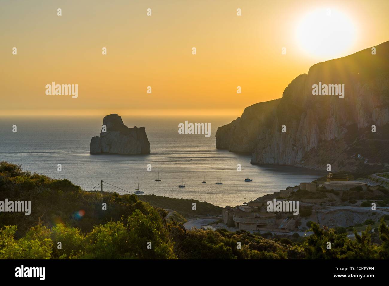 Il sole tramonta su una baia tranquilla, dipingendo il cielo in tonalità dorate. Le navi a vela navigano tranquillamente sull'acqua, catturando la bellezza della serata. Foto Stock