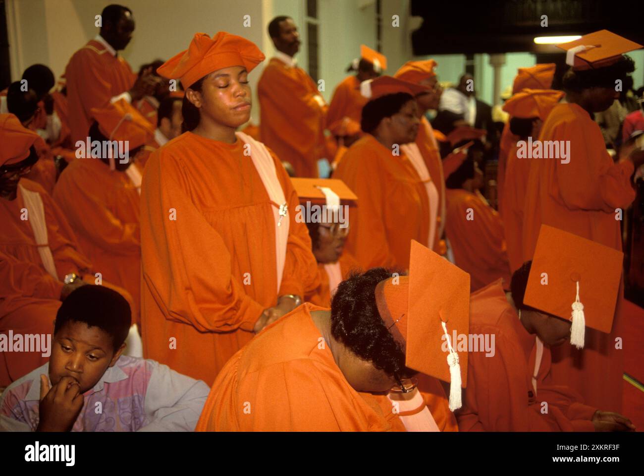 Brixton, Londra, Inghilterra intorno al 1990. La Chiesa Calvario di Dio in Cristo, i membri del coro pregano durante una funzione ecclesiastica domenicale. Un giovane membro della congregazione sua madre è nel coro sembra annoiato. Foto Stock