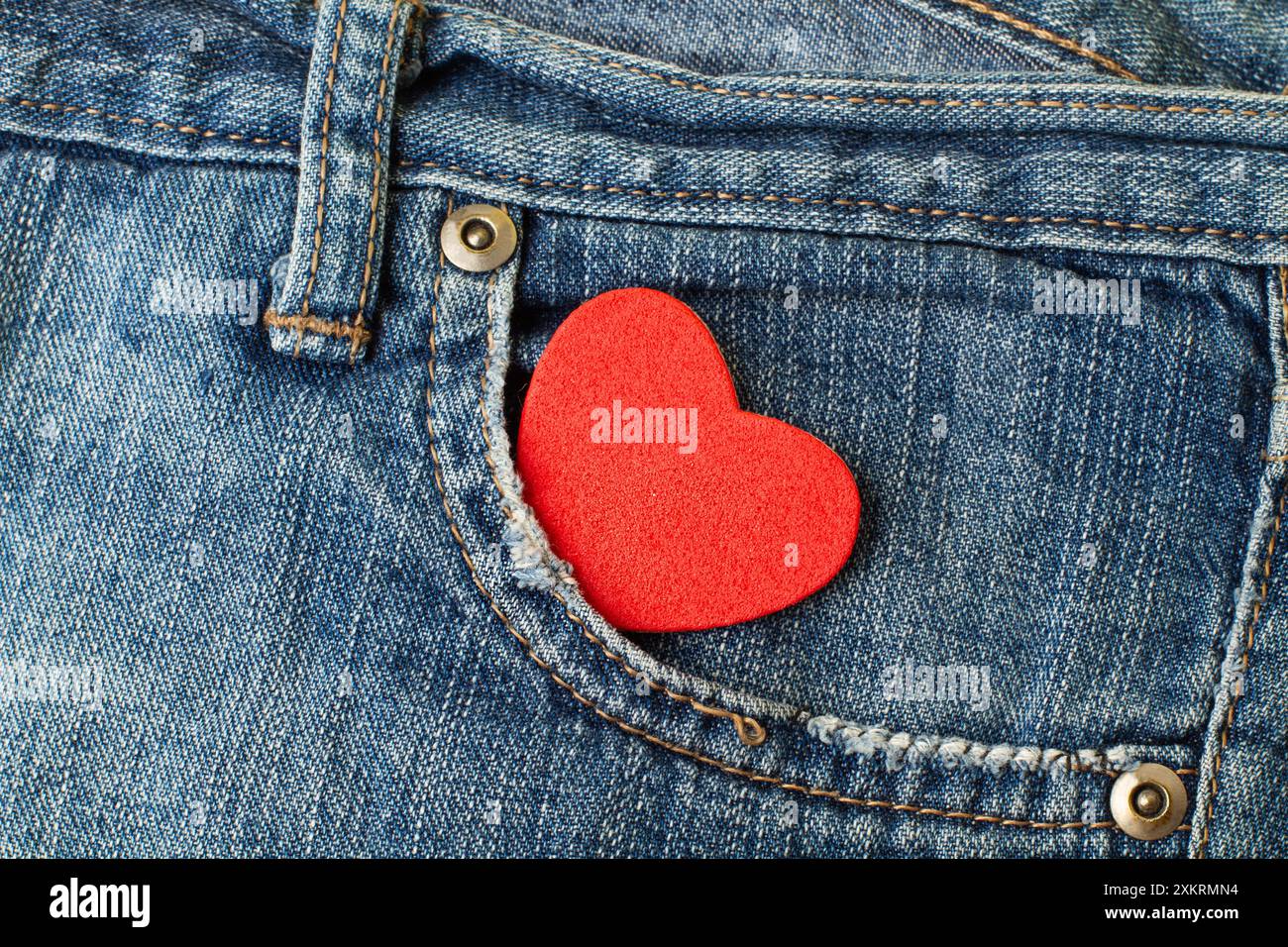 Un cuore rosso nella tasca di un pantalone blu in jeans con vista ravvicinata Foto Stock