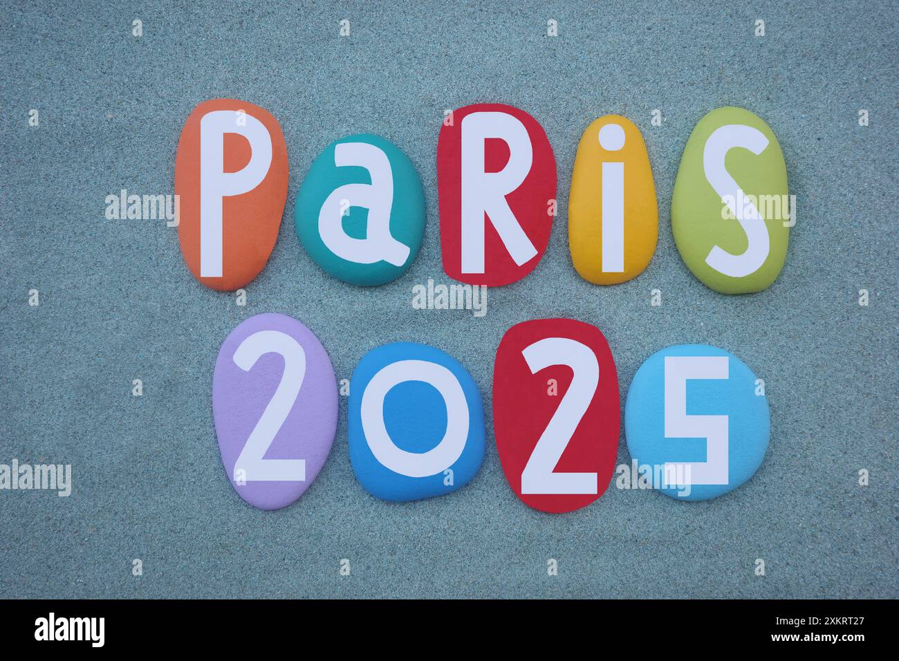 Paris 2025, logo creativo composto da lettere in pietra multicolore dipinte a mano su sabbia verde Foto Stock