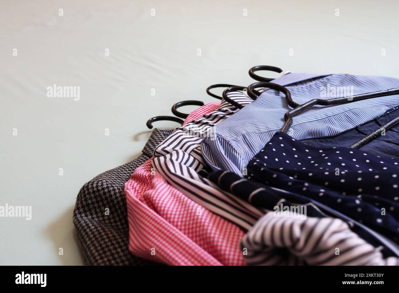 Abiti nelle tonalità blu, rosso, nero e bianco in diverse stampe ancora sull'appendiabiti impilati su uno sfondo chiaro. Foto Stock