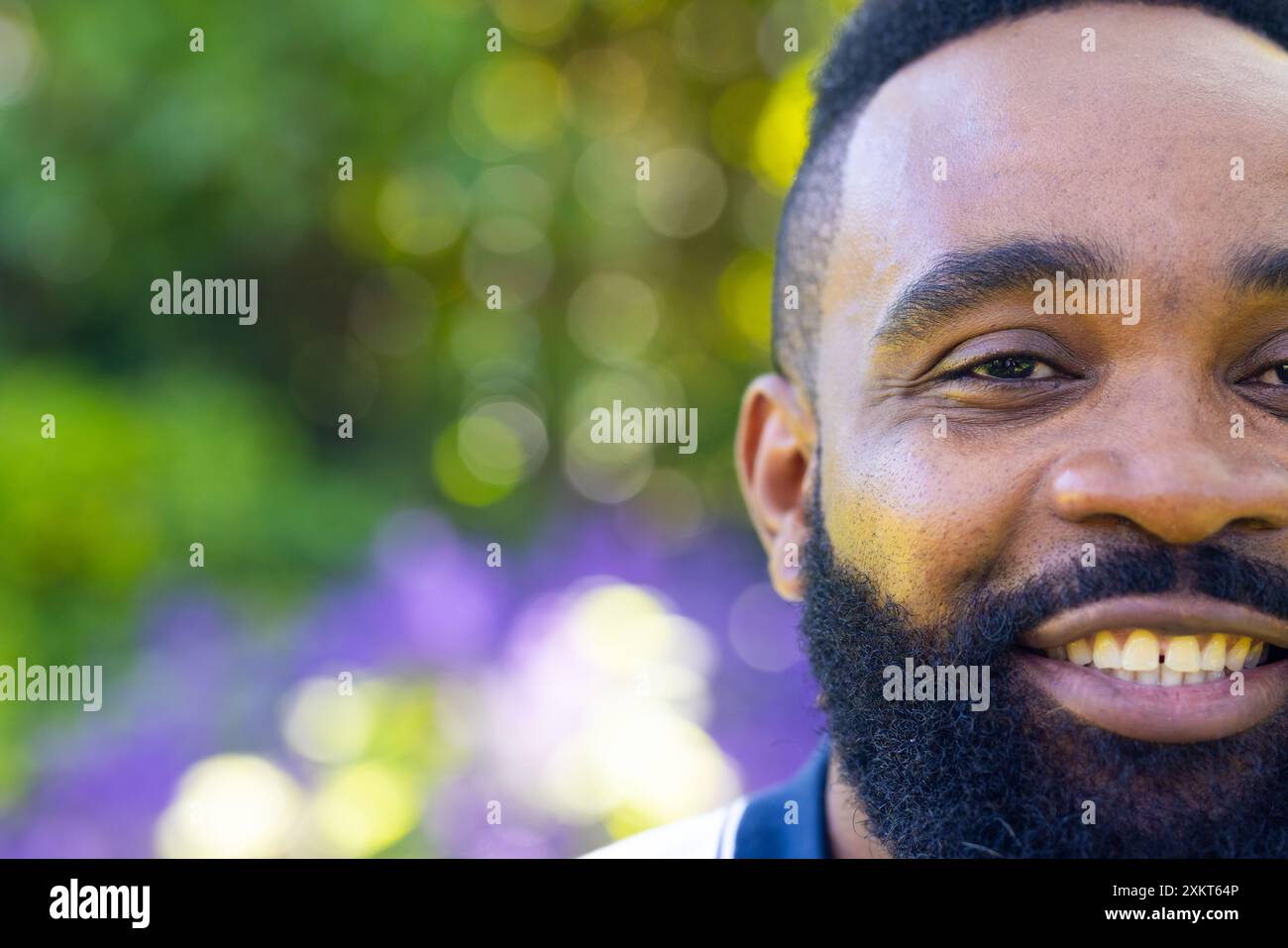 Sorridente uomo afroamericano all'aperto con sfondo naturale sfocato, godendosi una giornata di sole Foto Stock