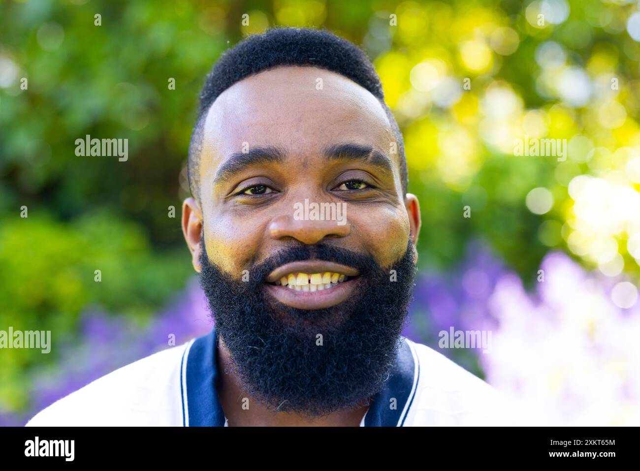 Uomo sorridente con la barba che si gode il giardino all'aperto, guardando la macchina fotografica Foto Stock