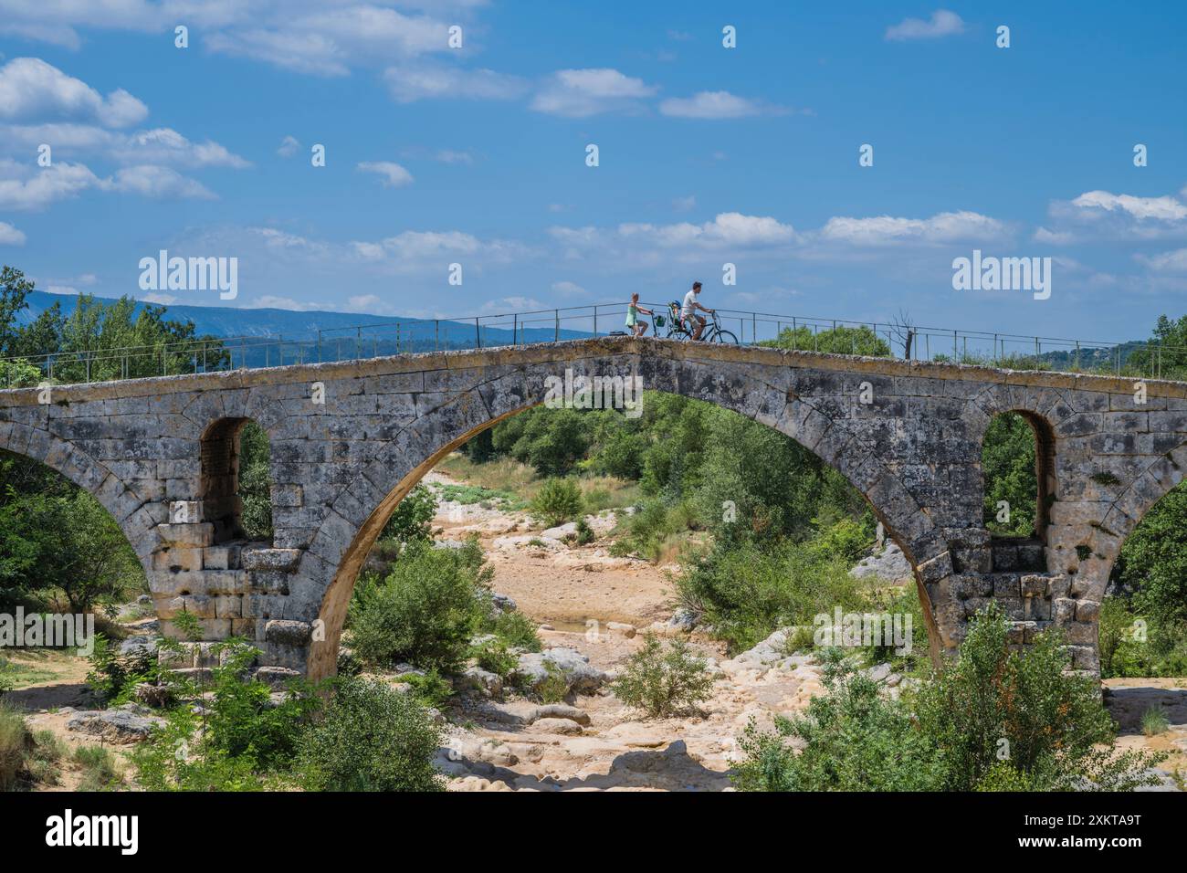 Una famiglia che pedala sul ponte romano vecchio di 2000 anni, Pont Julien, vicino a Bonnieux, Vaucluse, Francia. Foto Stock