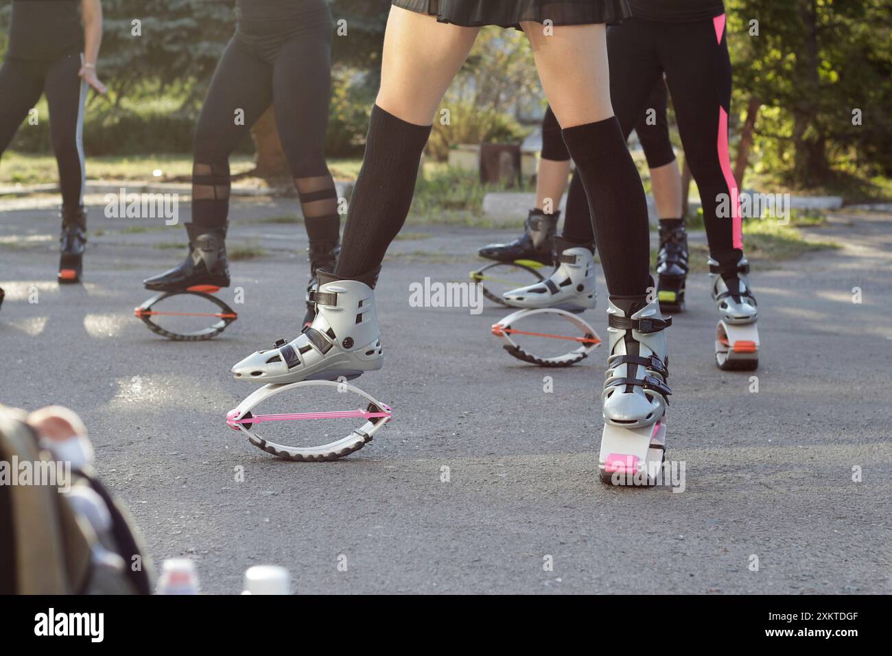 Attività sportive all'aperto kangu jumping gruppo di donne nel cortile del parco estivo, persone in stivali saltatori leggings calze al ginocchio. senza faccia, vista dal basso Foto Stock