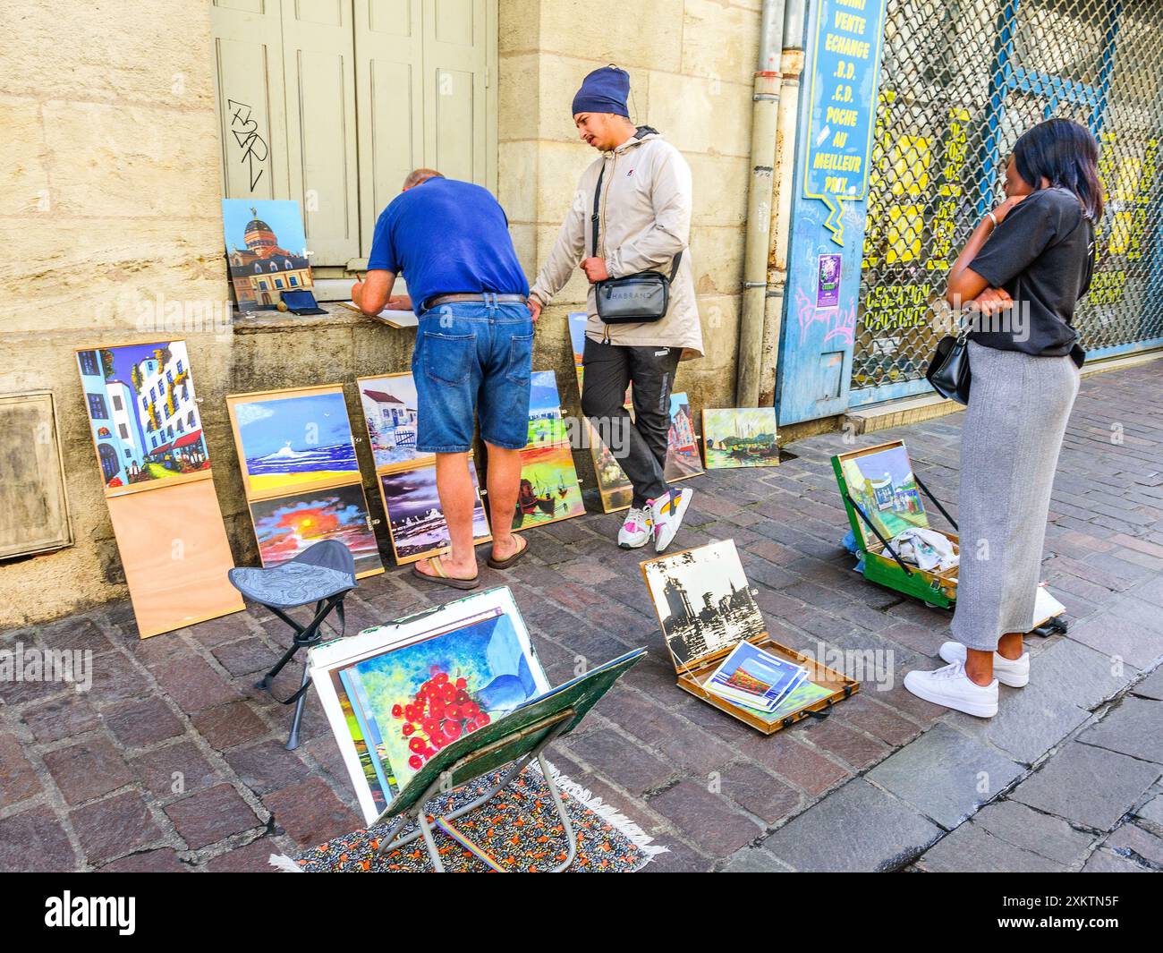 Artista dilettante con opere d'arte disposte sul marciapiede che discutono l'arte con persone in strada - Tours, Indre-et-Loire (37), Francia. Foto Stock