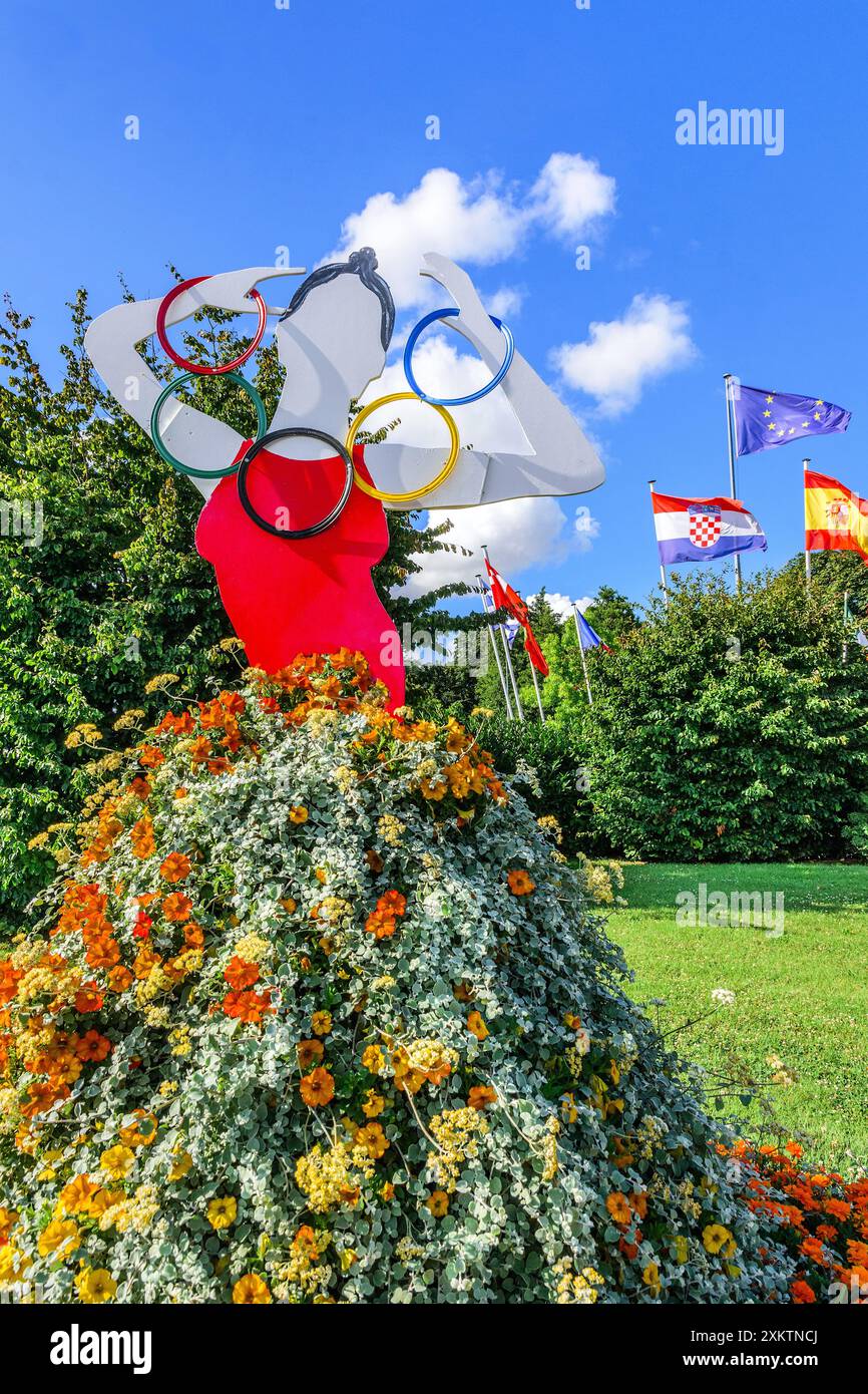 Immagine di donna con gonna floreale che regge il simbolo degli anelli olimpici sulla rotonda del traffico - Cartesio, Indre-et-Loire (37), Francia. Foto Stock