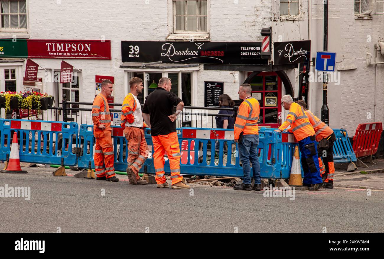 Un gruppo di operai edili in abiti ad alta visibilità in piedi intorno a un'area scavata in una strada, discutendo dei lavori in corso. Marlborough Wilts Foto Stock