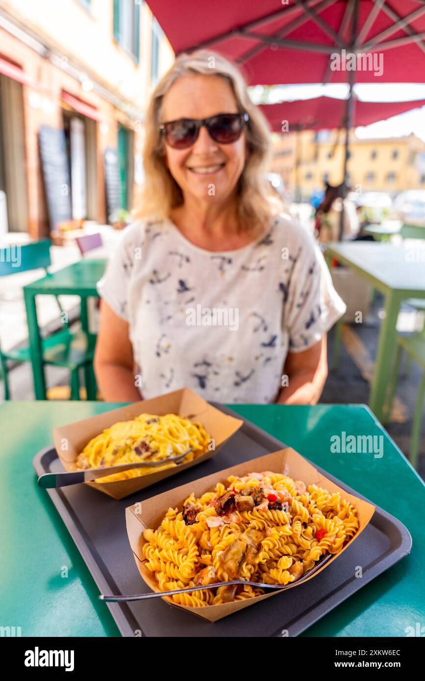 Una turista di mezza età si siede per Un pranzo a base di pasta presso Un caffè a Pisa, in Toscana, in Italia. Foto Stock