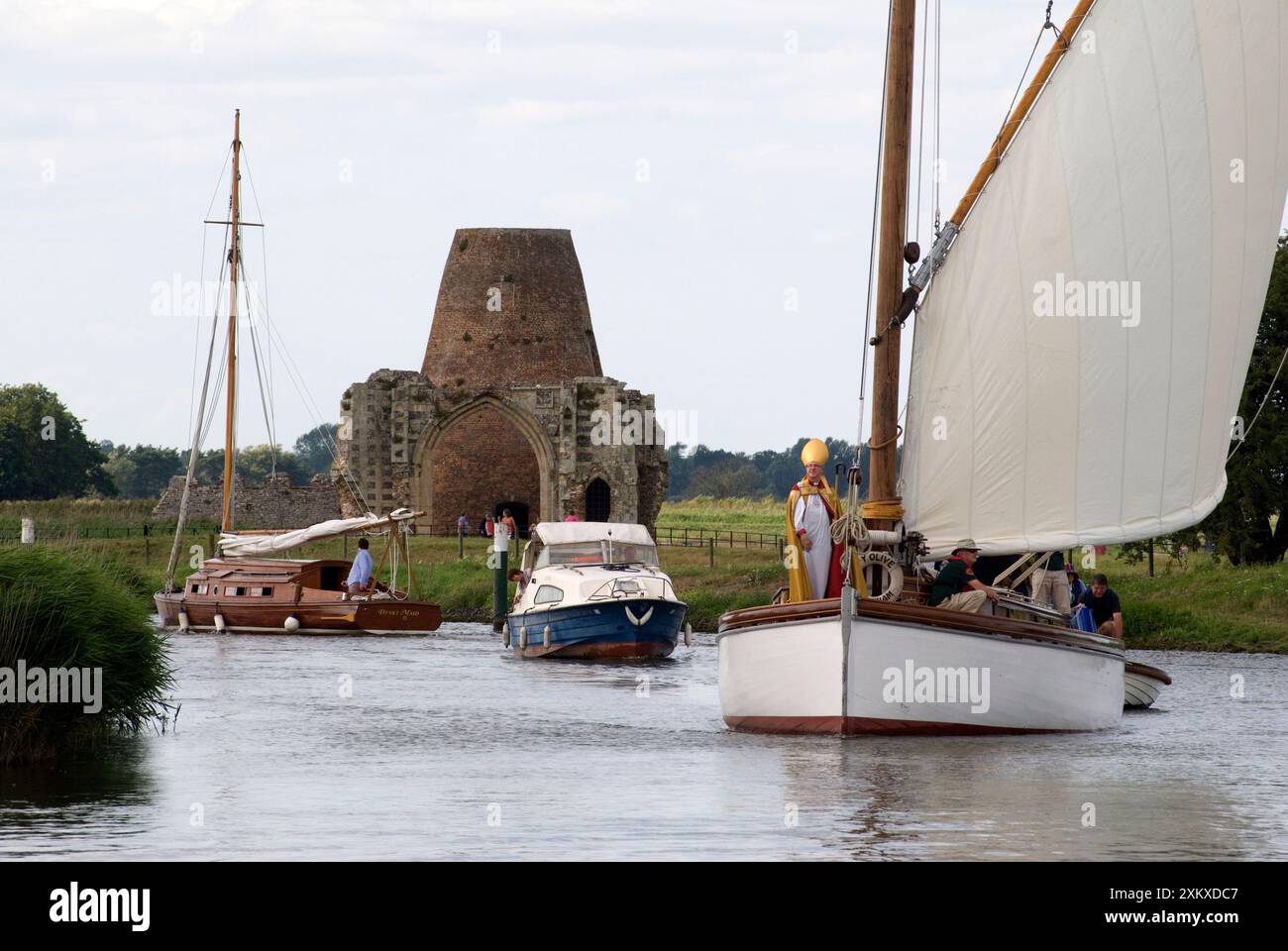 Norfolk Broads Wherry. Il vescovo di Norwich il reverendo Graham James arriva da Wherry, una tradizionale barca a vela di Norfolk Broads per prendere un servizio interconfessionale presso le rovine dell'abbazia (sullo sfondo) di St Benets. Ludham Norfolk Regno Unito. La prima domenica di agosto ogni anno. Inghilterra anni '2014 2010 Regno Unito HOMER SYKES Foto Stock