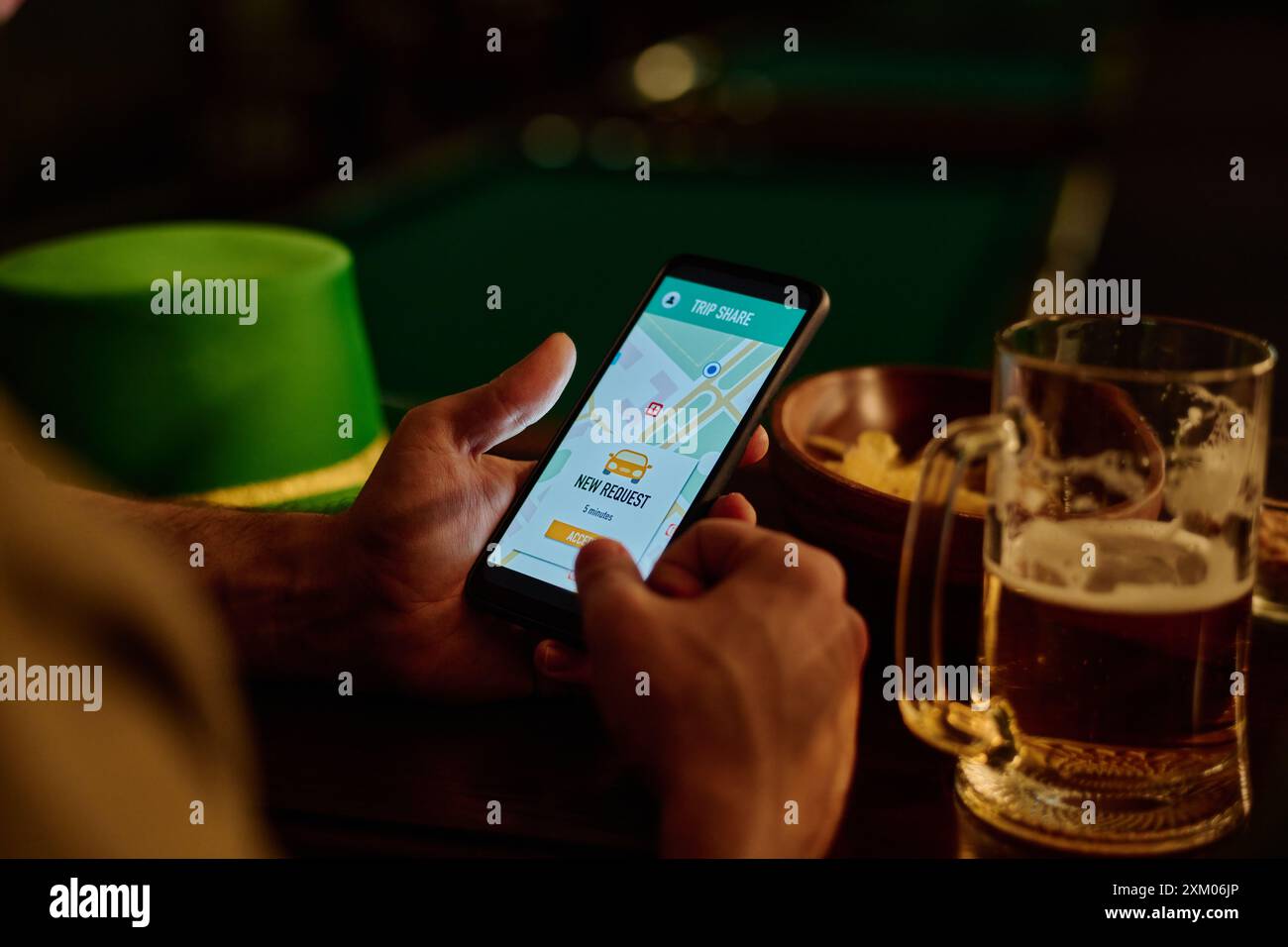 Smartphone con sistema di condivisione del viaggio sullo schermo in mano a un giovane uomo riposante che chiama un taxi seduto accanto al bancone del bar con una tazza di birra Foto Stock