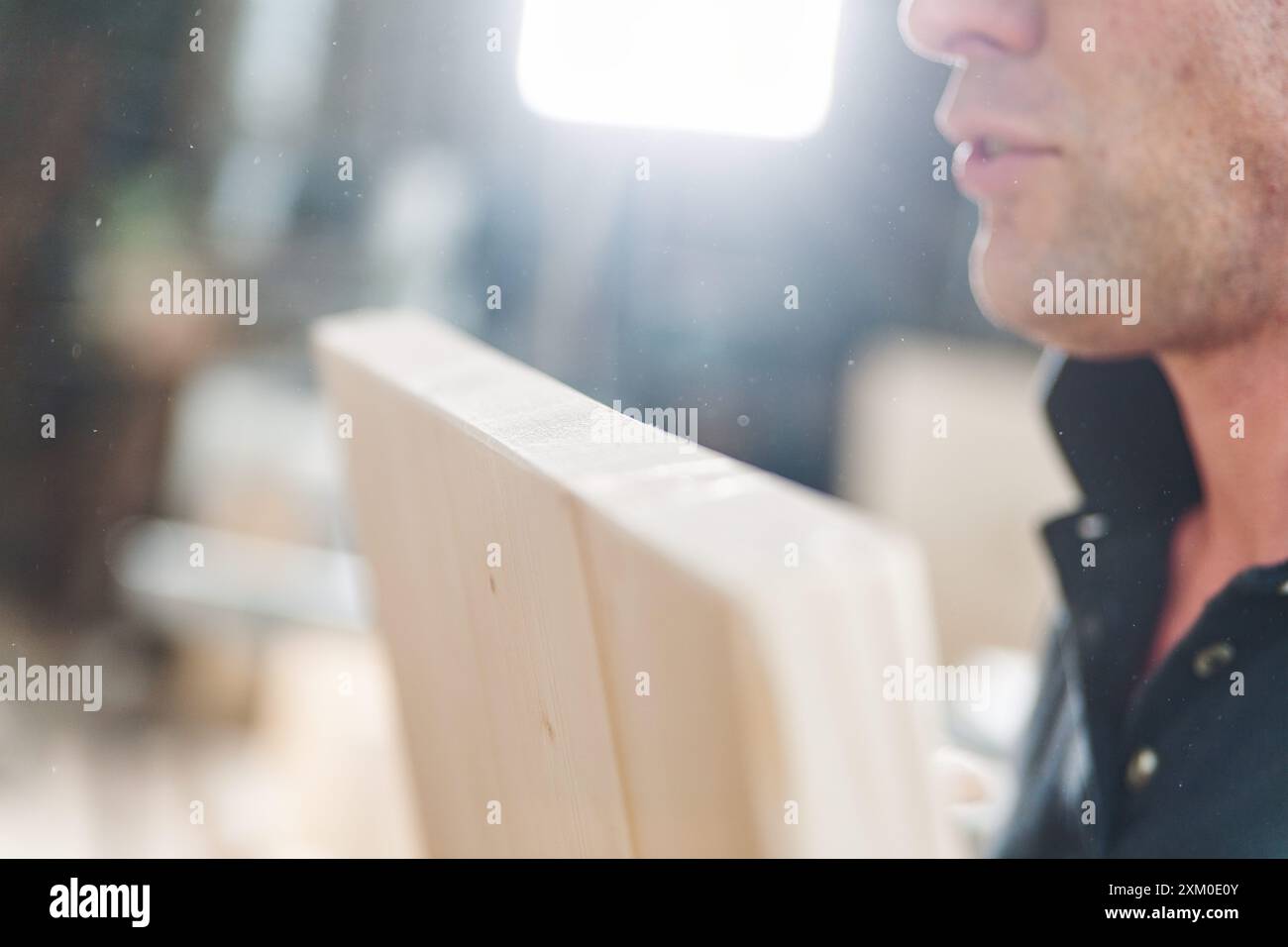 Carpenter sta analizzando una tavola di legno in un'officina, con particelle di segatura visibili nell'aria, evidenziando la maestria artigianale Foto Stock