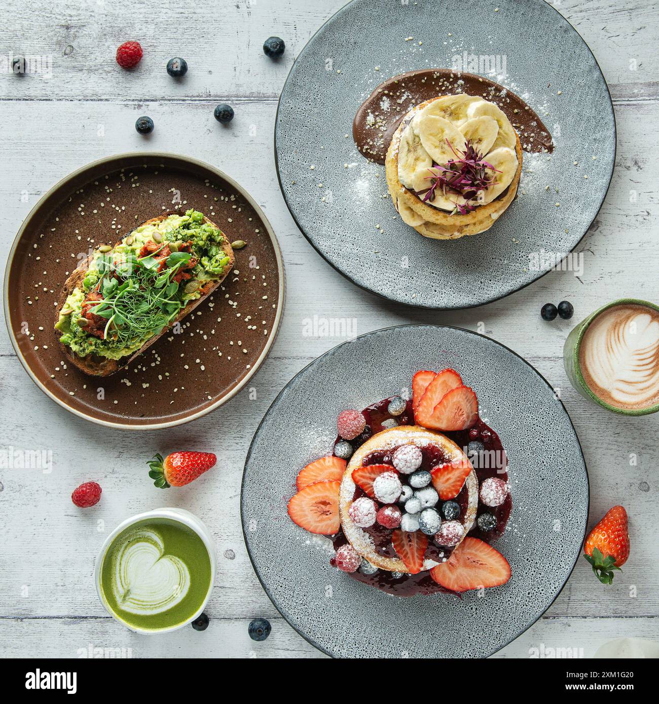 Pancake di frutta, pancake alla banana e toast all'avocado con caffè e latte matcha, sul tavolo del bar. Foto Stock