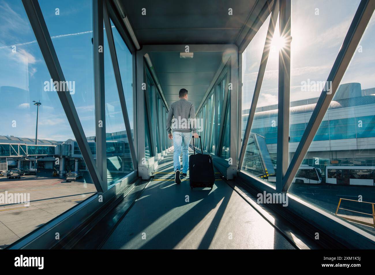 Viaggio in aereo. Vista posteriore dell'uomo con bagaglio a mano che cammina sul ponte d'imbarco dei passeggeri all'aeroporto nelle giornate di sole. Foto Stock