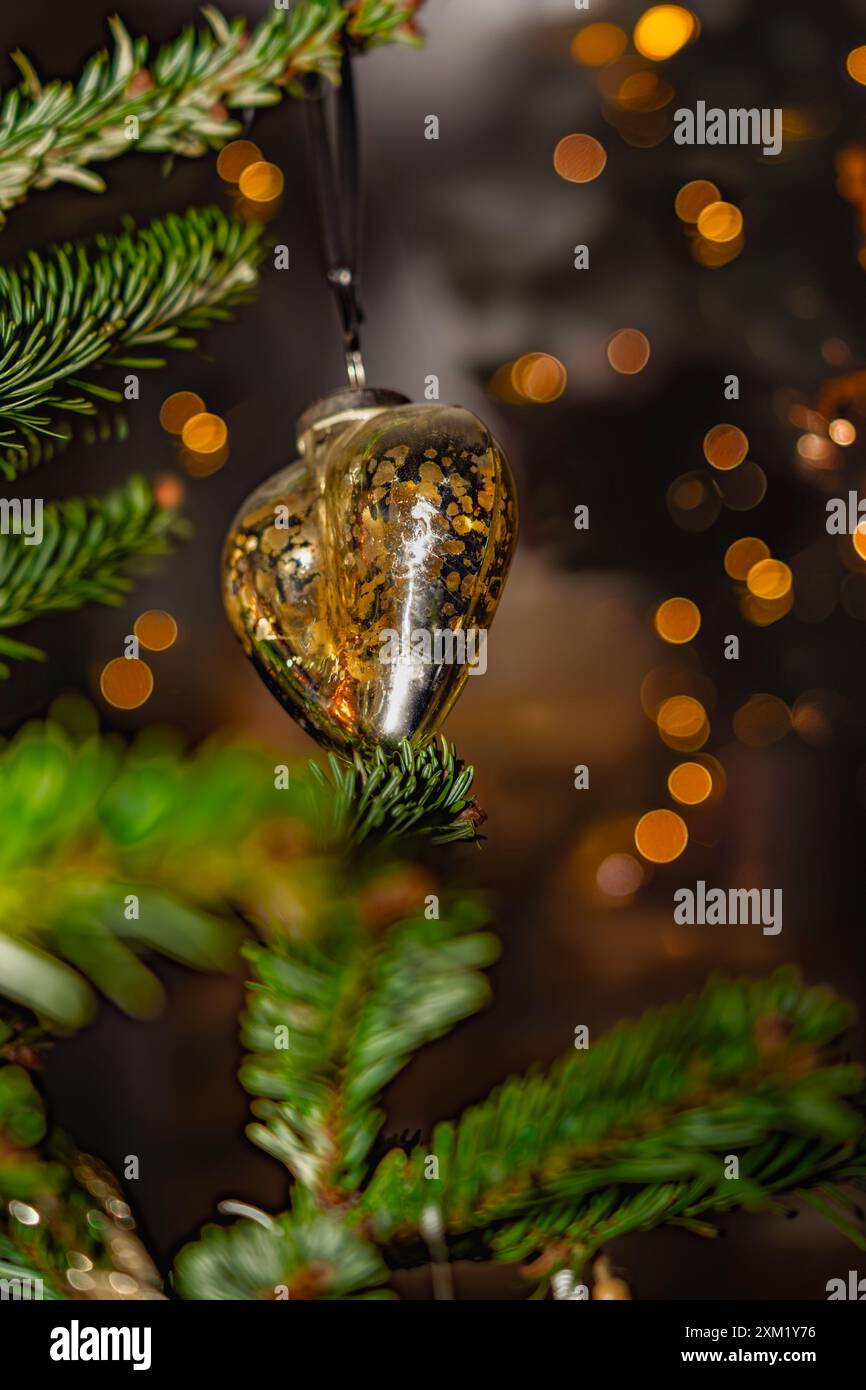 Un ornamento a forma di cuore dorato in rame è appeso su un ramo di pino, con luci natalizie sfocate sullo sfondo. Foto Stock