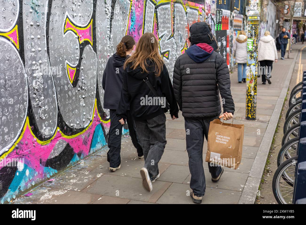 Gli adolescenti camminano lungo un muro ricoperto di graffiti, Londra Foto Stock