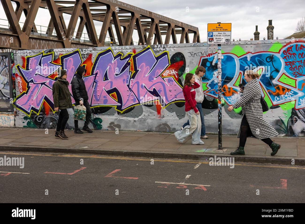 I pedoni camminano di fronte a un muro coperto di graffiti, Londra Foto Stock