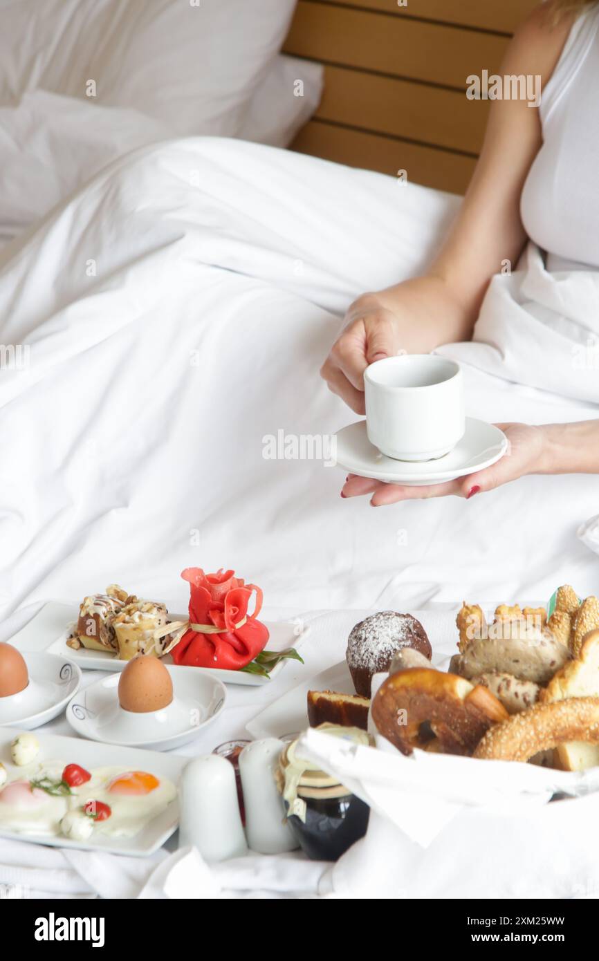 Giovane donna che fa colazione nel letto. Mattinata tranquilla e idilliaca a casa o in camera d'hotel Foto Stock