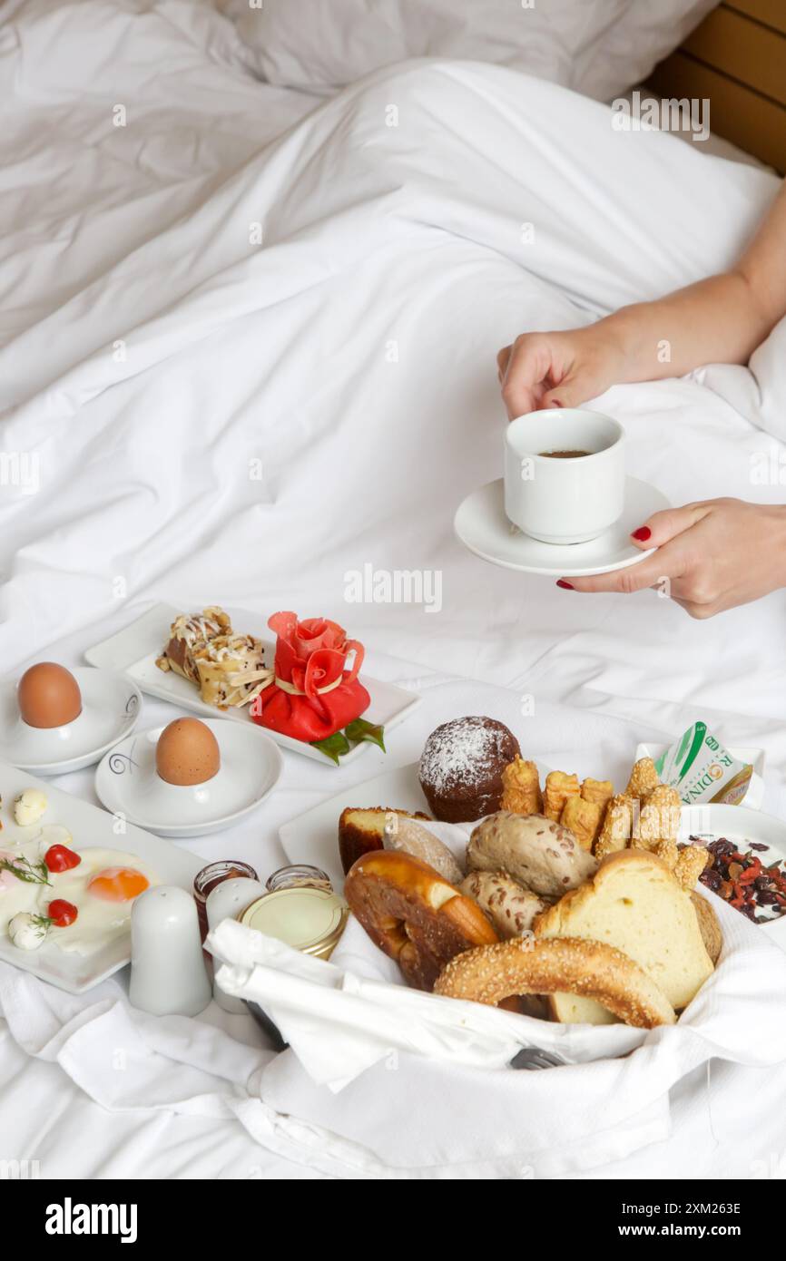 Giovane donna che fa colazione nel letto. Mattinata tranquilla e idilliaca a casa o in camera d'hotel Foto Stock