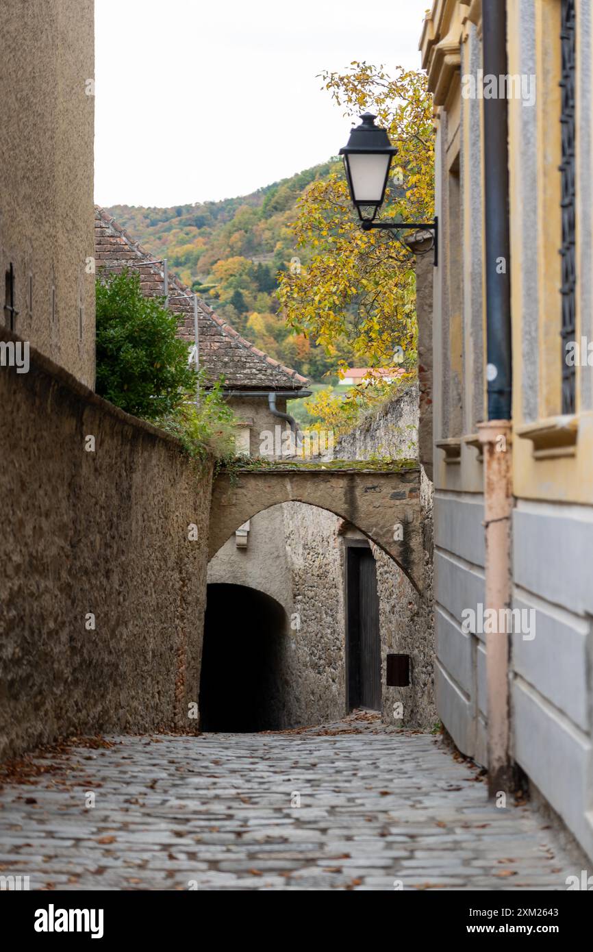 Vicolo acciottolato in Austria, con un'antica arcata in pietra che conduce ad un passaggio buio. Un lampione è appeso sopra la testa. Foto Stock