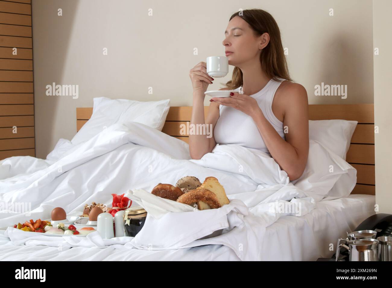 Giovane donna che fa colazione nel letto. Mattinata tranquilla e idilliaca a casa o in camera d'hotel Foto Stock