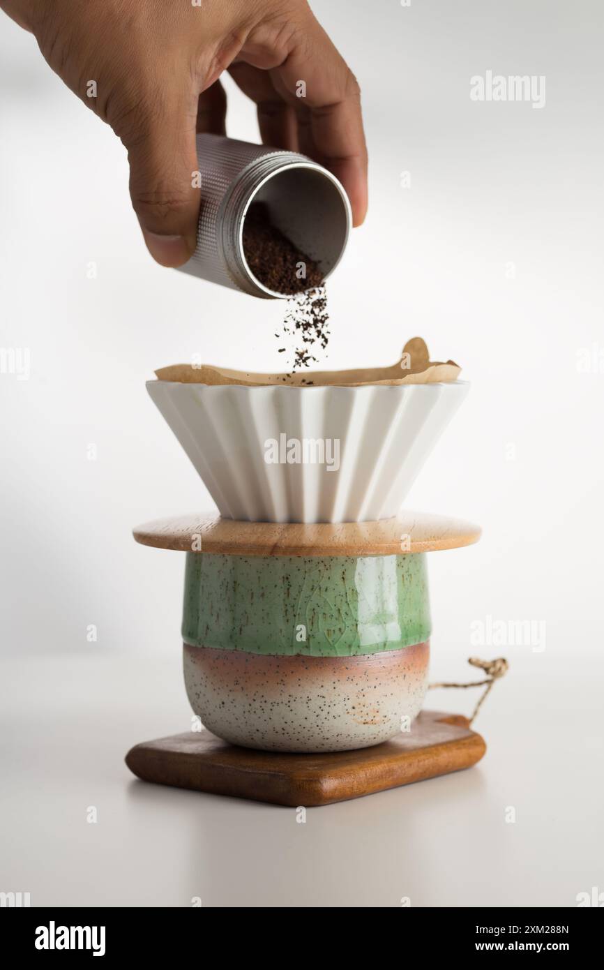 Una mano delicata fa cadere i fondi di caffè nel filtro di carta incontaminato, promettendo un'infusione aromatica. Foto Stock