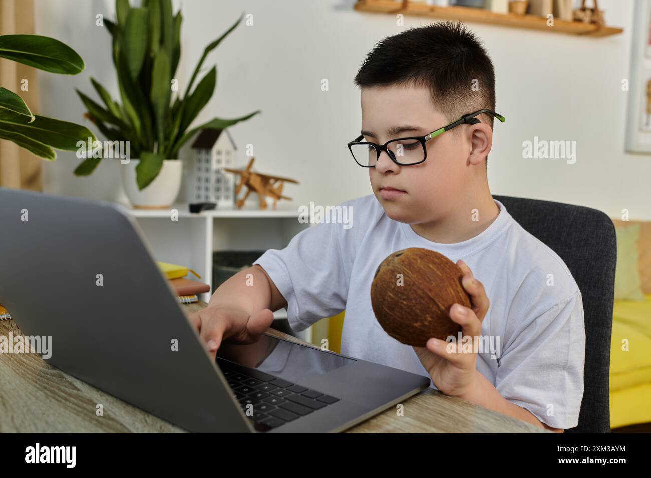 Ragazzo con sindrome di Down alla scrivania con laptop, che tiene la noce di cocco. Foto Stock