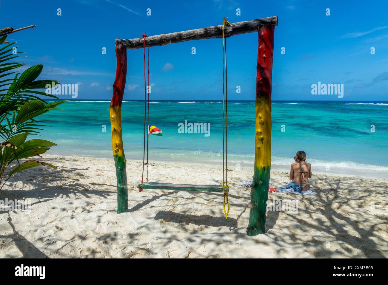 Donna seduta vicino a un'altalena colorata sulla scenografica spiaggia di sabbia tropicale Anse Source d'Argent, l'isola di la Digue, Seychelles Foto Stock